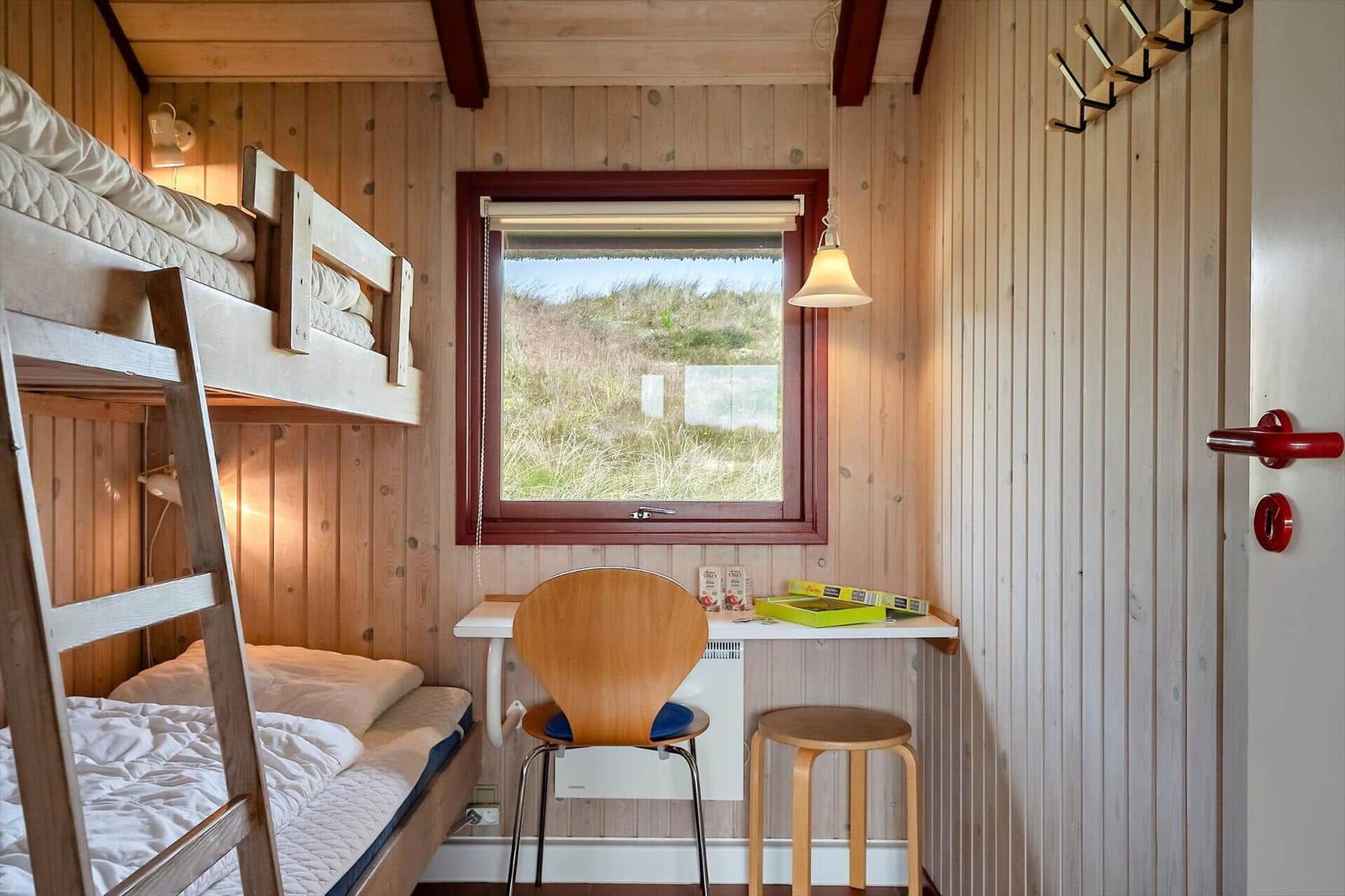 Kleines Schlafzimmer mit Doppelstockbett, Schreibtisch und Fensterblick auf Grasland.