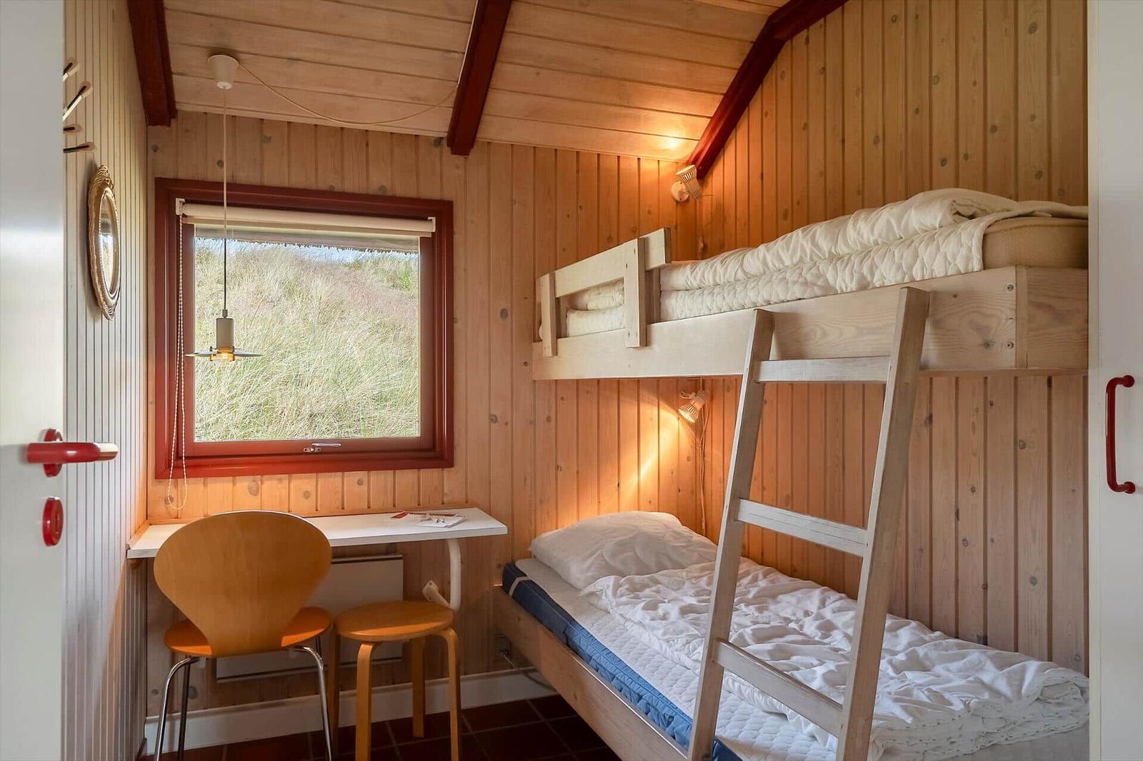Zimmer mit Doppelstockbett, Schreibtisch und Fenster mit Blick auf Gras.