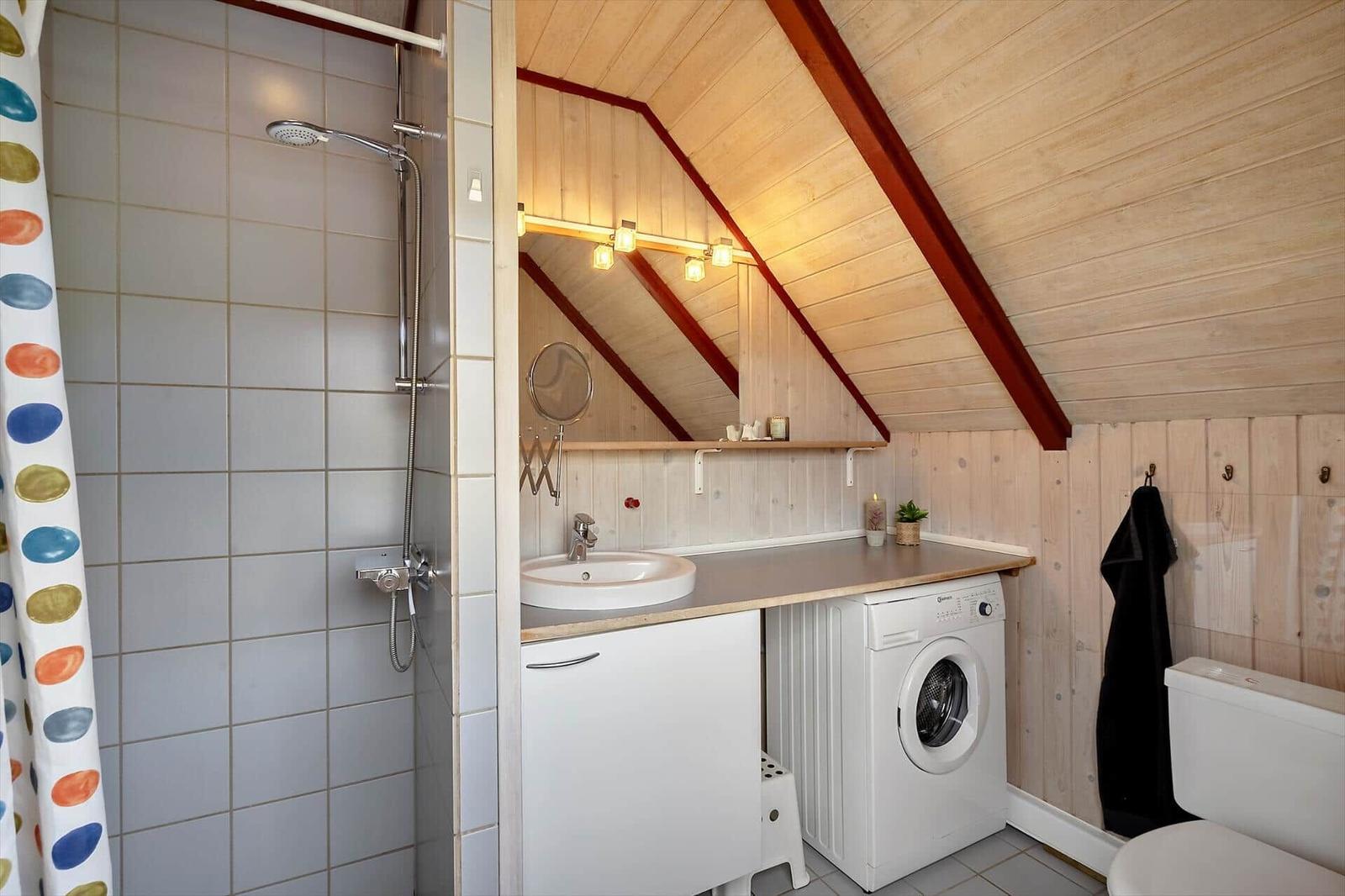 Badezimmer mit Dusche, Waschbecken und Waschmaschine unter Dachschrägen.