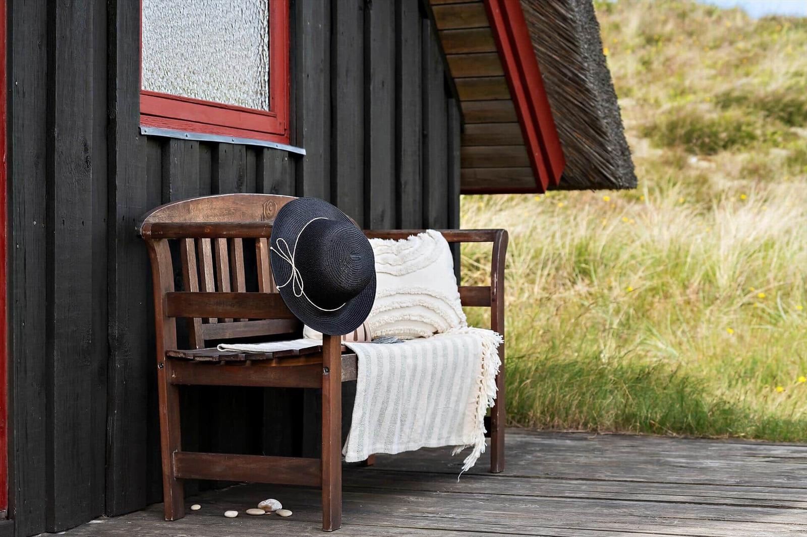 Holzbank vor einem dunklen Haus mit Strohdach, darauf liegt ein Hut und eine Decke.