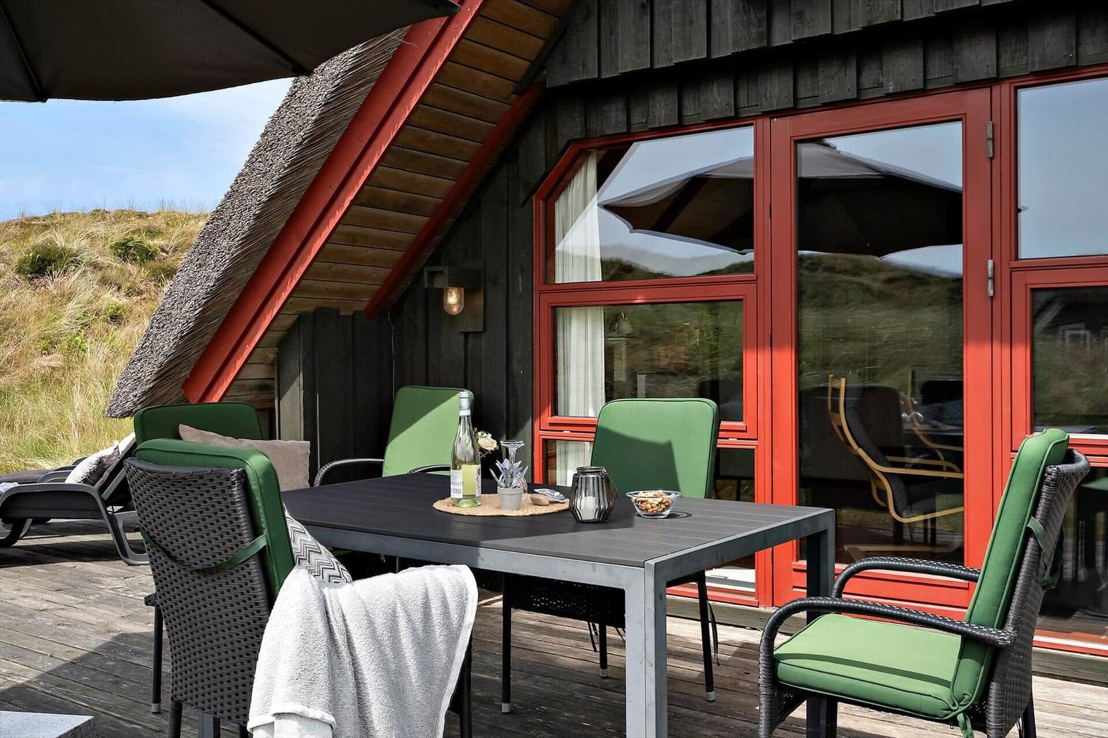 Terrasse mit Tisch, grünen Stühlen und Blick auf grasbewachsene Hügel.