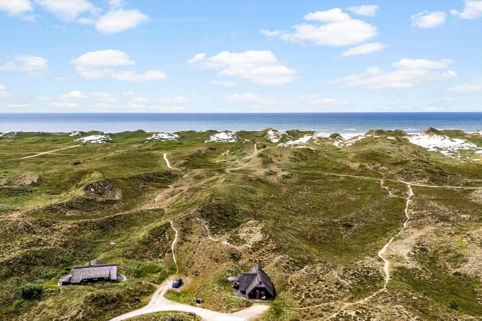 Zwei Häuser auf grünen Dünen mit Blick auf das Meer unter blauem Himmel.