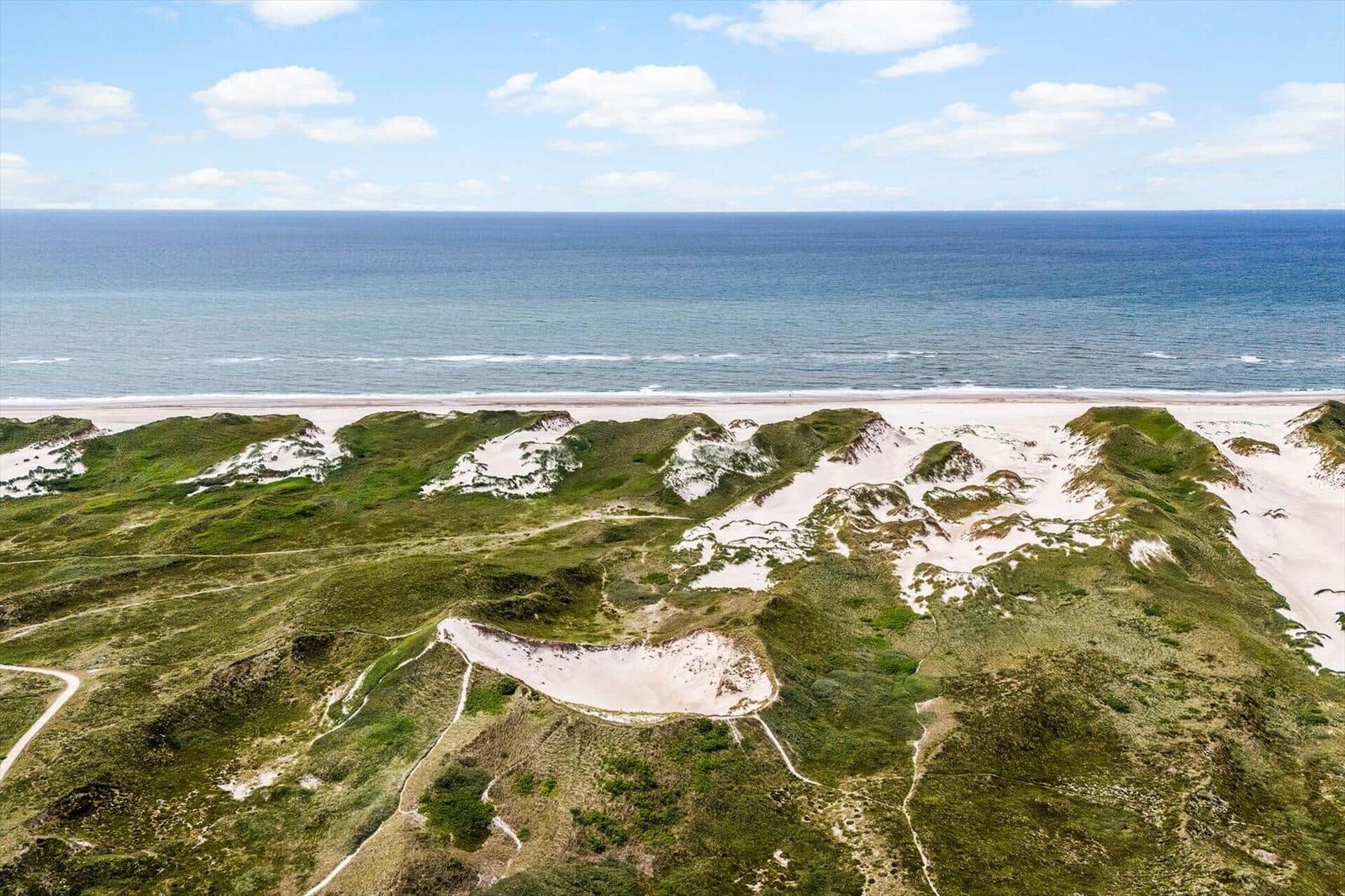 Ausblick auf Strand und Meer mit grünen Dünen und sandigen Hügeln.