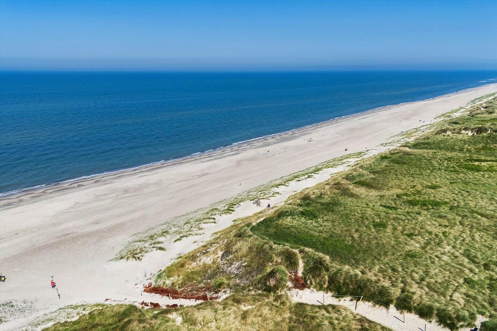 Strand mit Dünen und blauem Meer unter klarem Himmel.