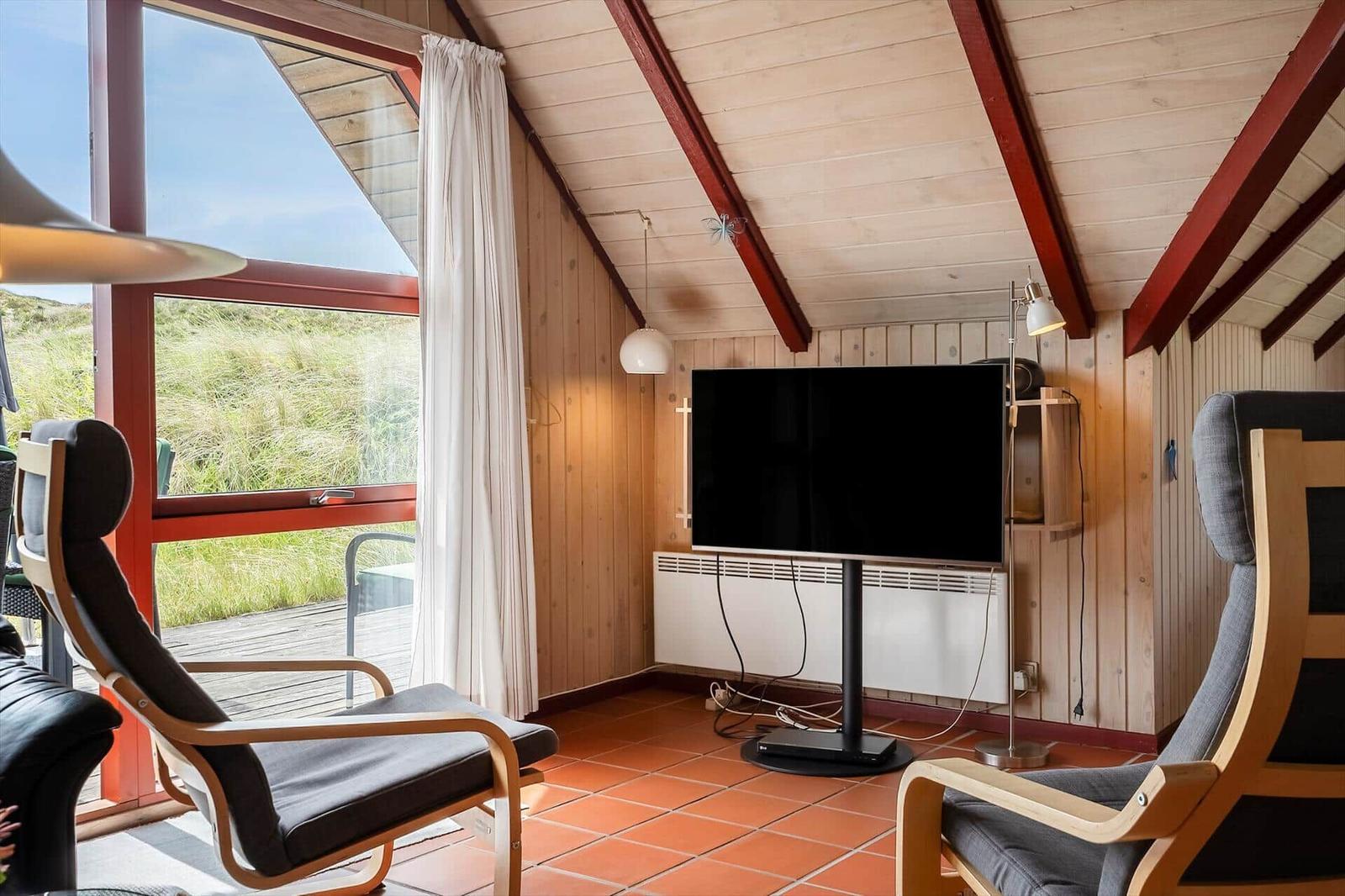 Zimmer mit Fernseher, zwei Sesseln und Blick auf Grasflächen.