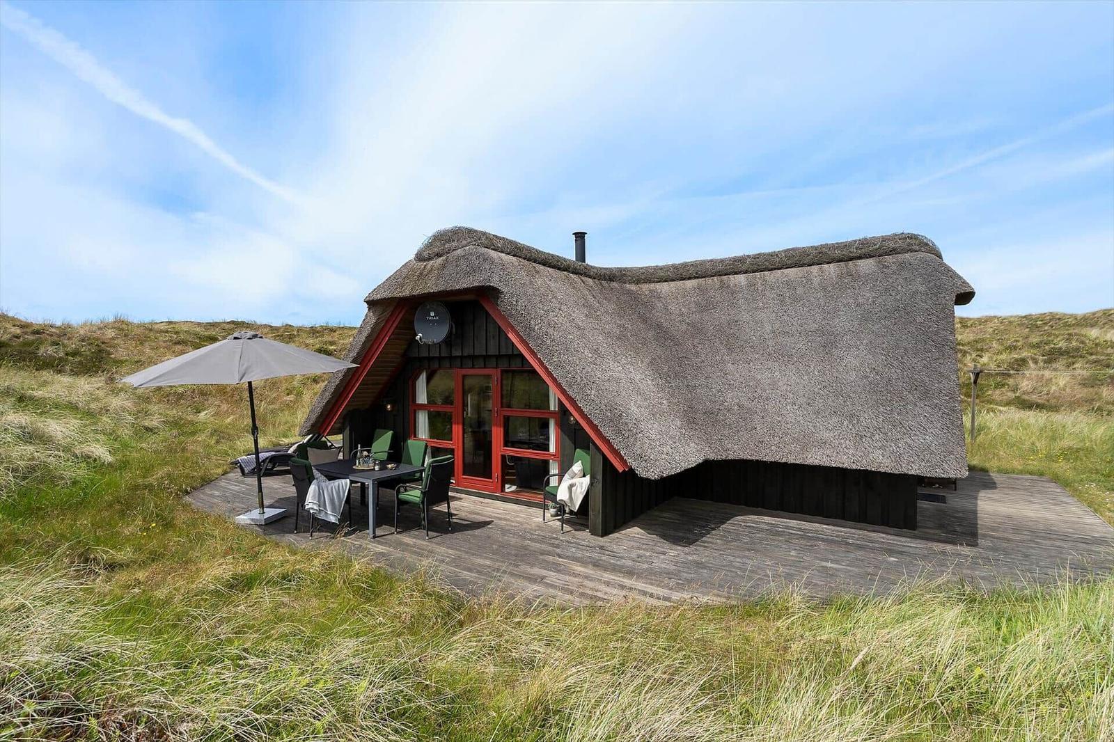 Hütte mit Strohdach und Holzterrasse im Grasland.