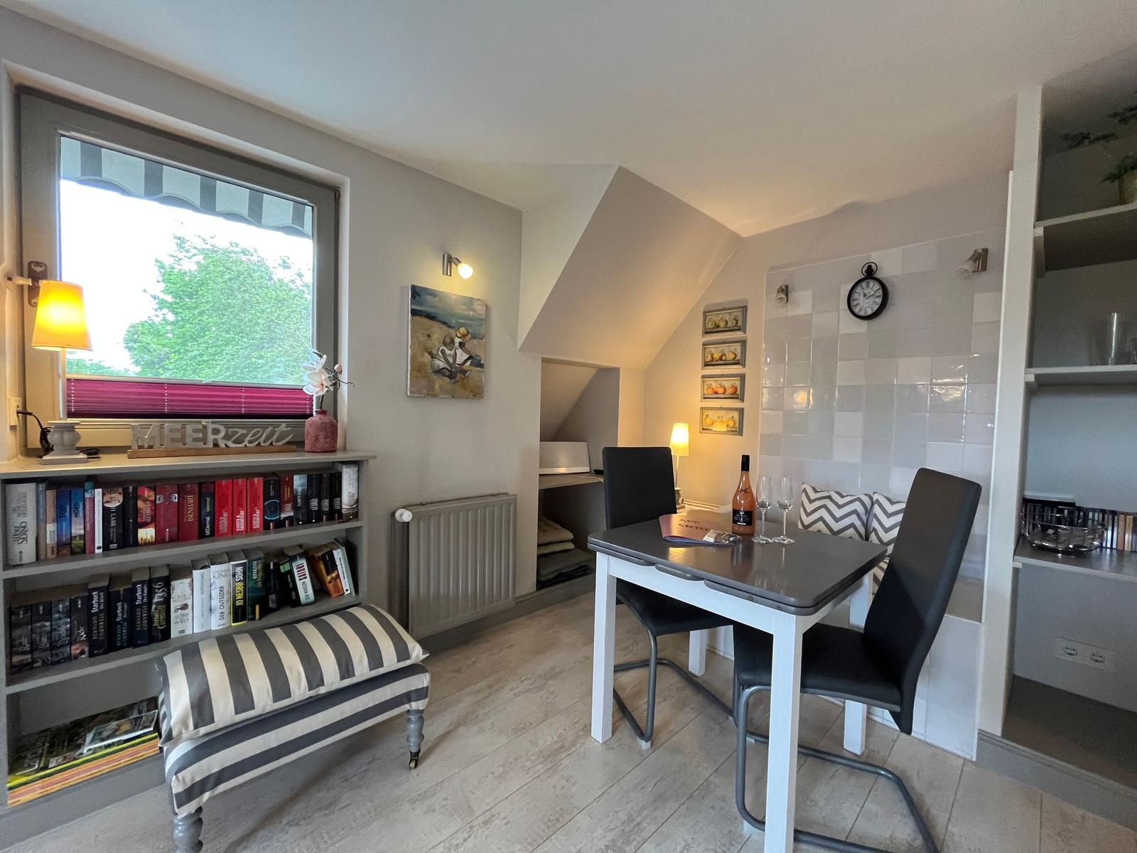 Room with table, chairs, bookshelf, and window with view of green.