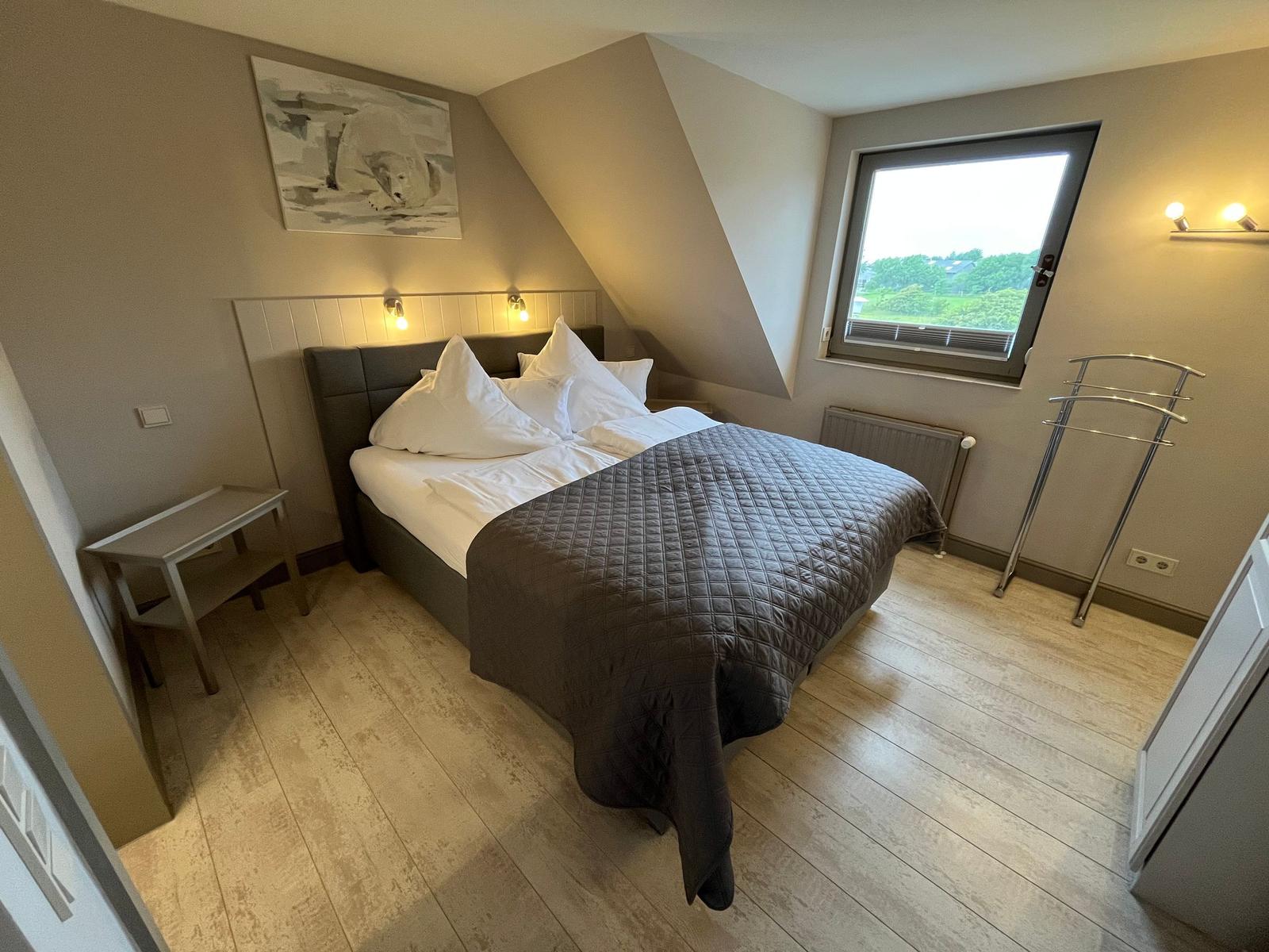 Bedroom with sloped ceiling, bed, window, and clothes rack.