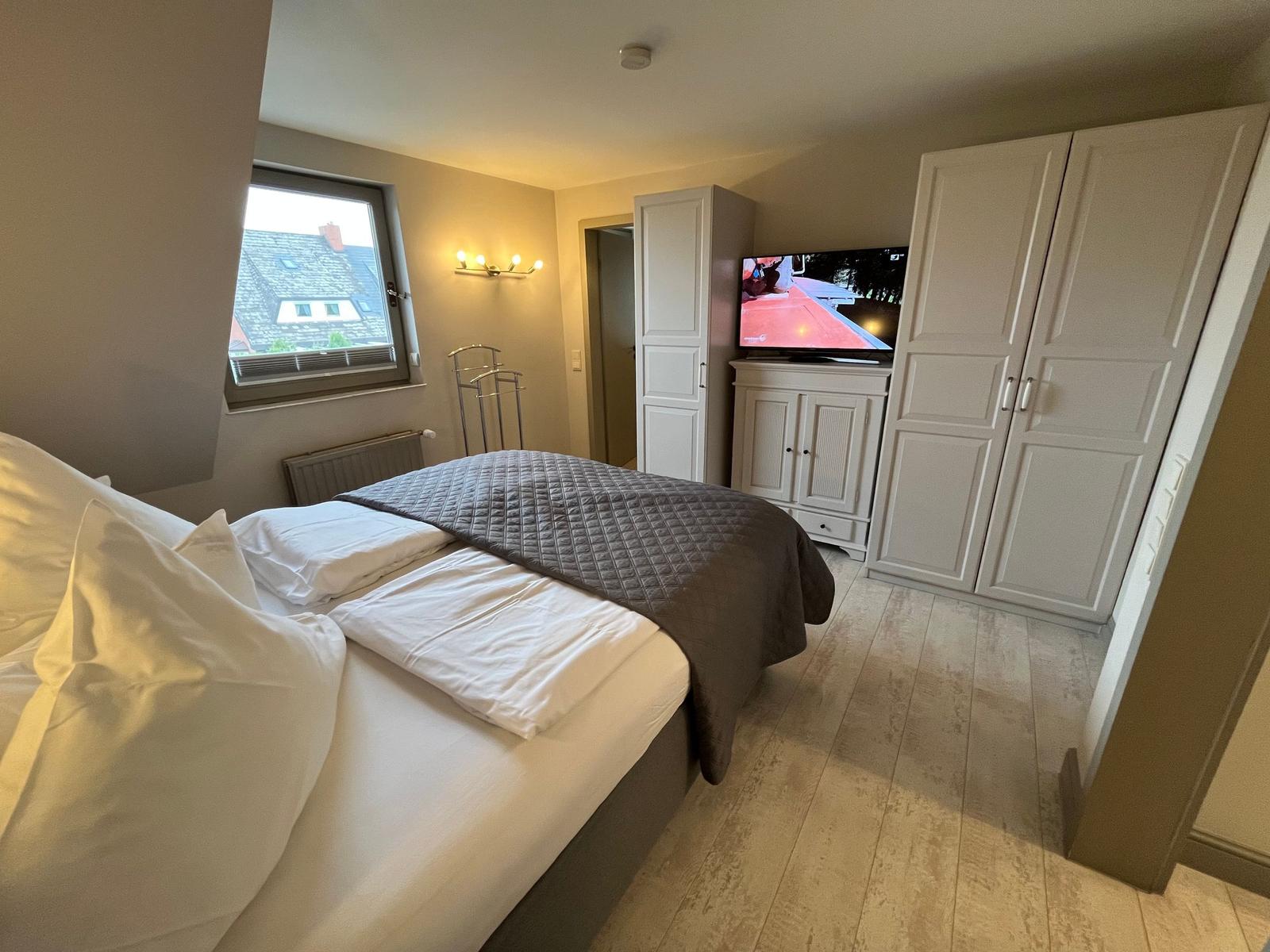 Bedroom with bed, TV, and wardrobe. Window with view of roof.