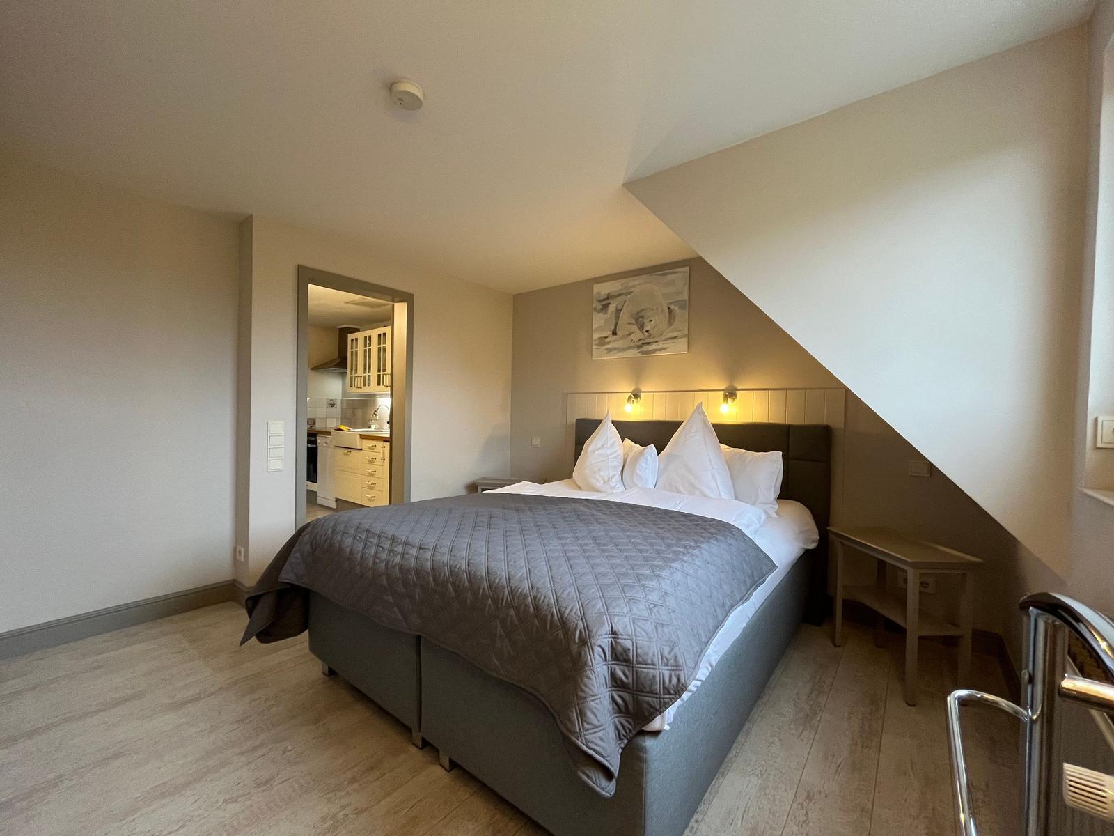 Bedroom with double bed, adjacent kitchen, and sloped ceiling.