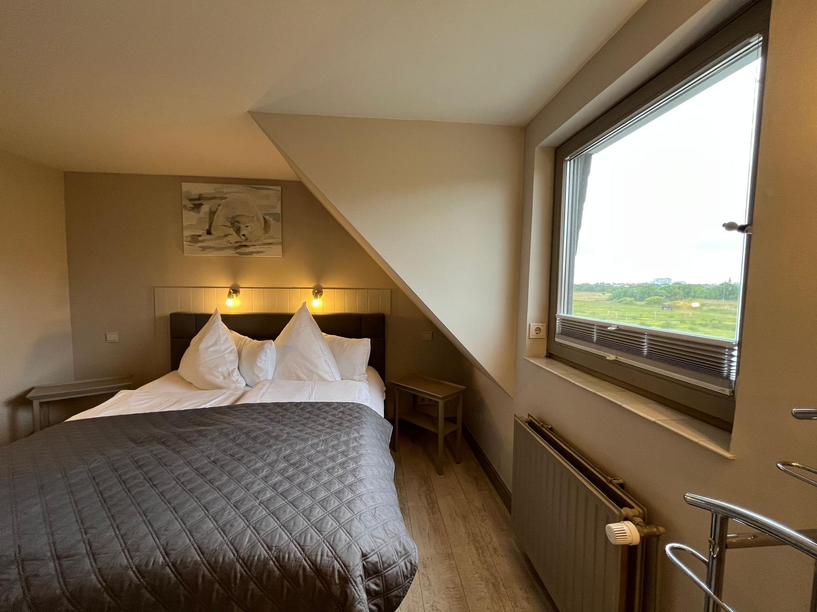 Bedroom with sloped ceiling, large window, and bed with gray quilt.