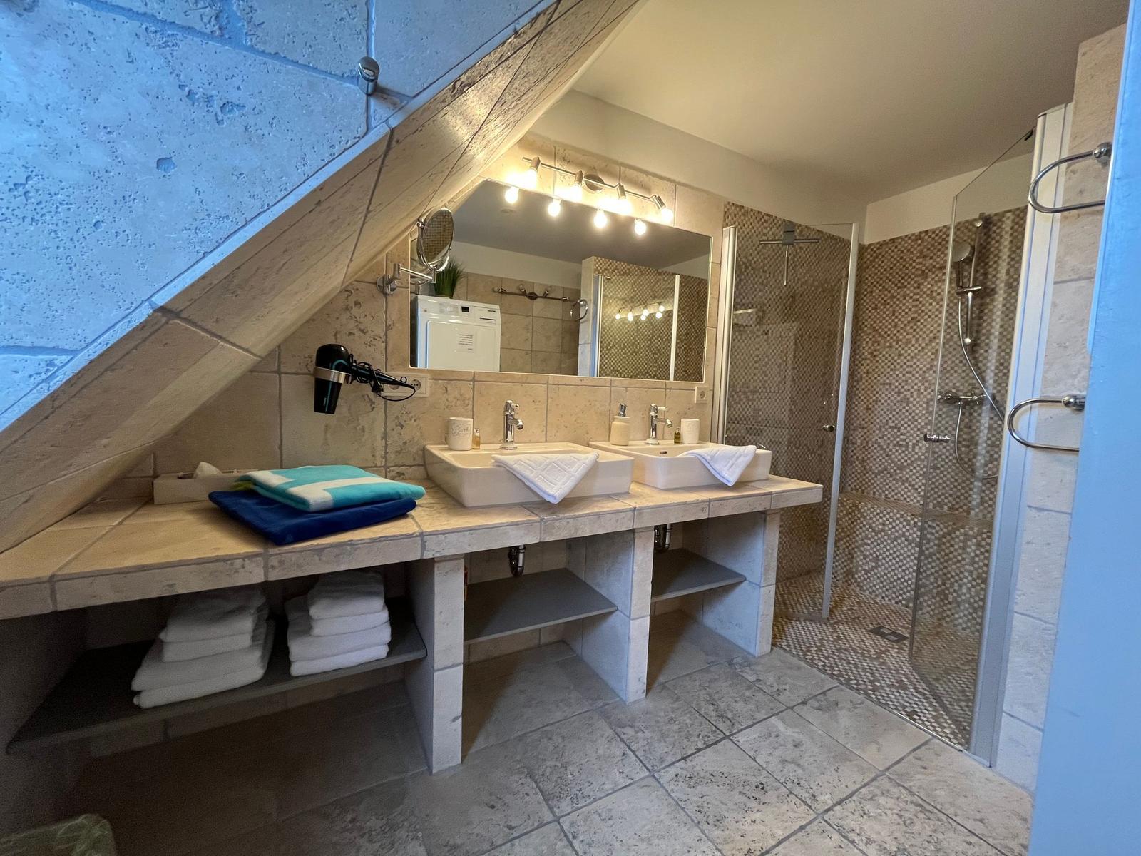 Bathroom with shower, two sinks, and towel racks under sloped ceiling.