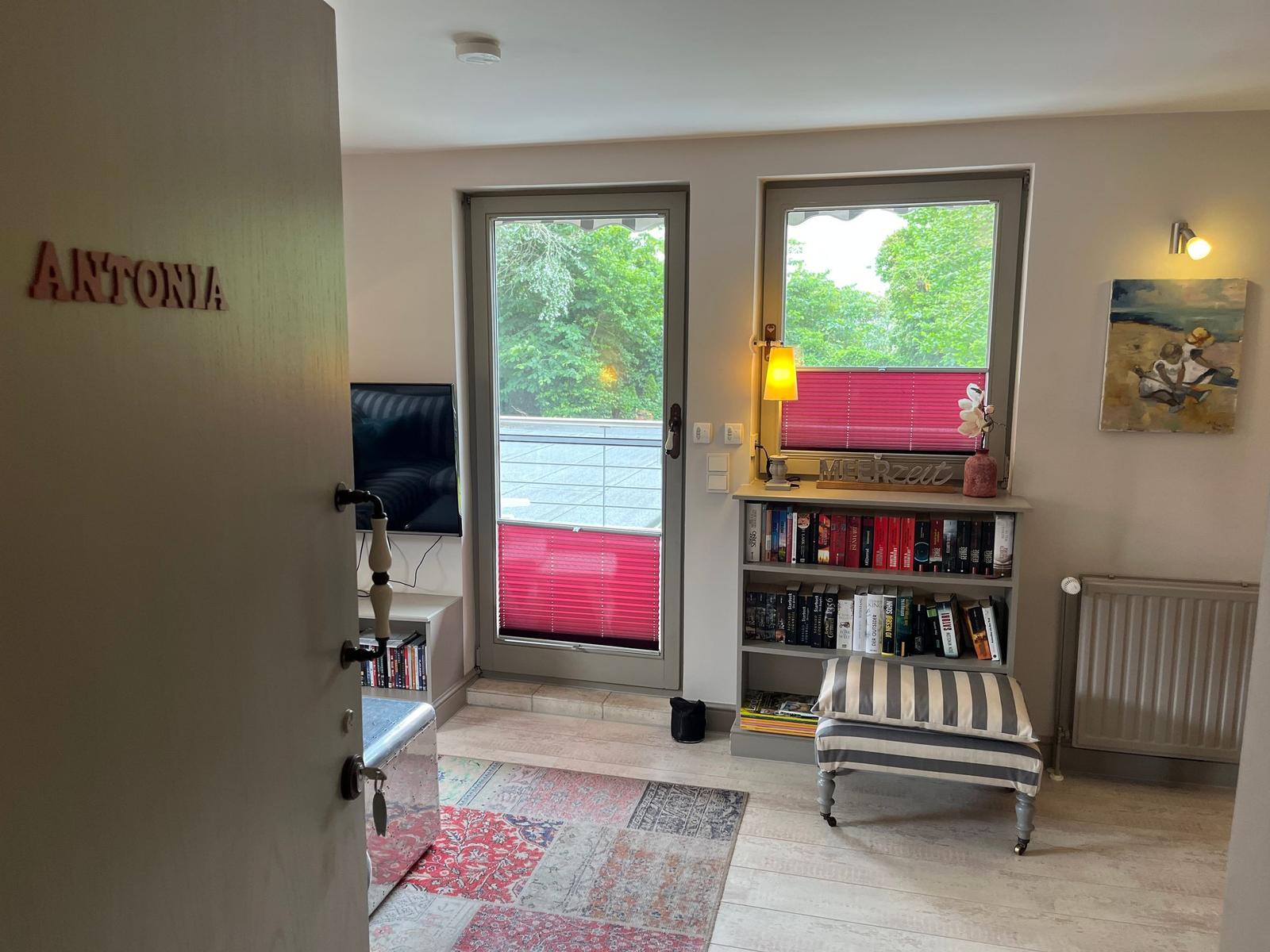Entrance area with door to apartment Antonia, bookshelf, windows, and balcony door.
