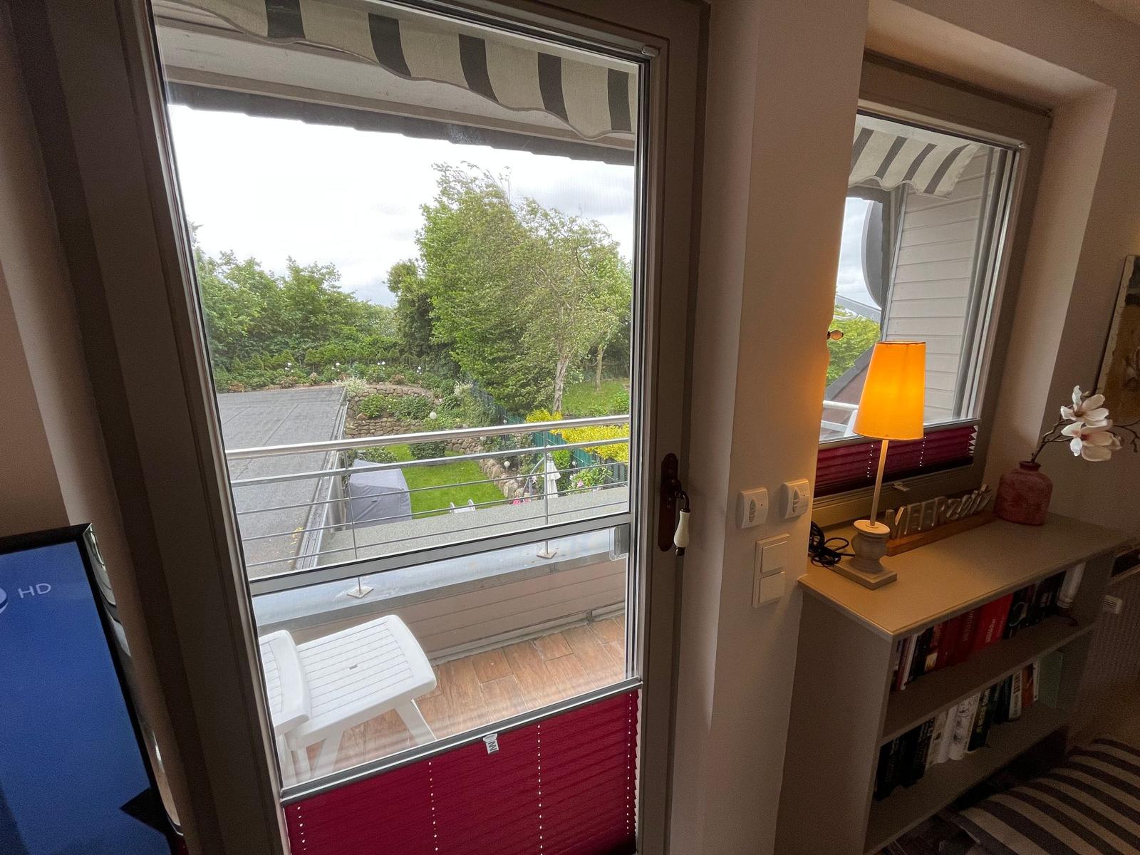 Through the glass door, a terrace with a chair and view of green trees is visible.