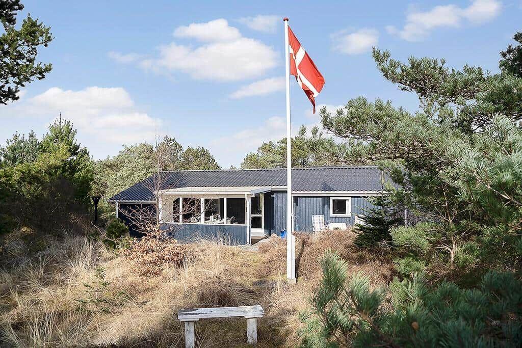 Ein blauer Holzhaus mit Flagge und Terrasse umgeben von Bäumen und Gras.