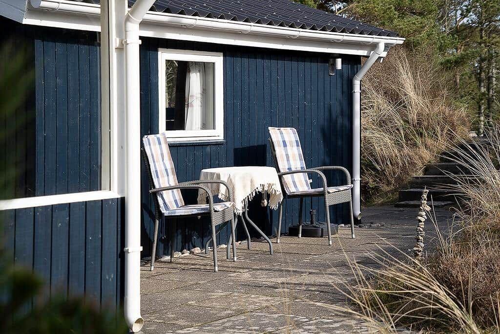 Außenbereich mit Tisch und zwei Stühlen vor einem blauen Holzhaus.