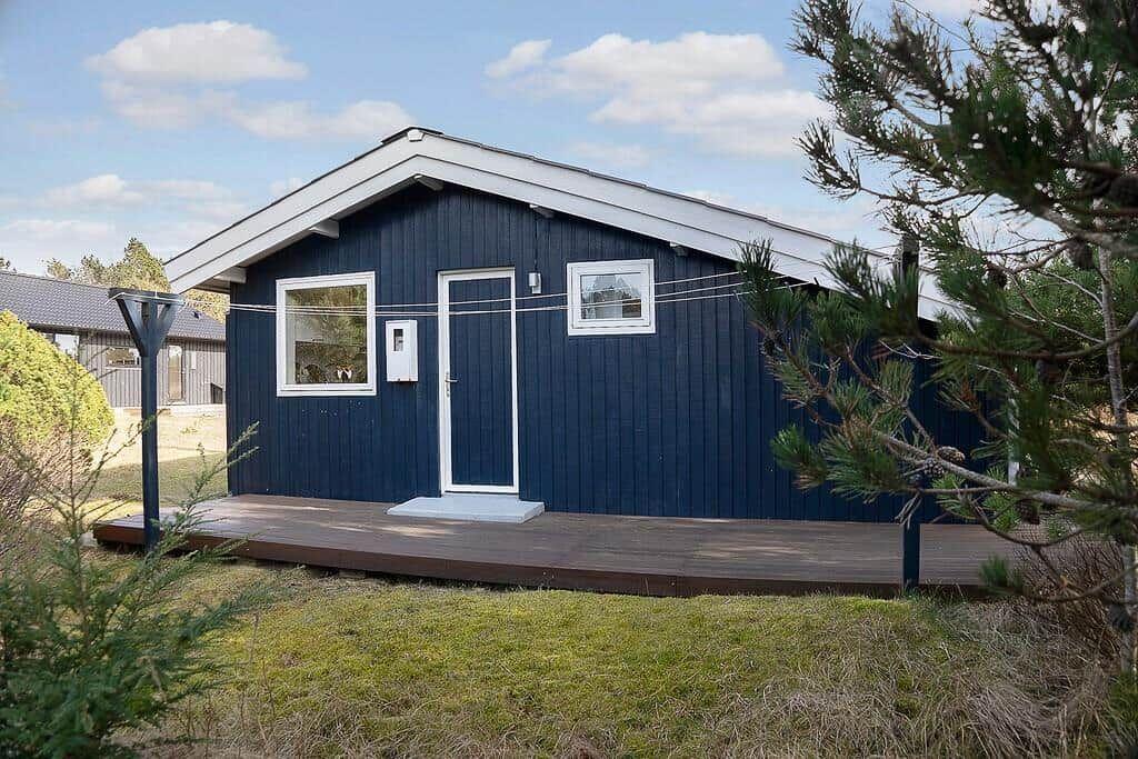 Blau gestrichenes Haus mit Holzterrasse und Fenstern. Umgeben von Gras und Bäumen.