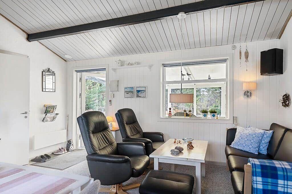 Wohnzimmer mit zwei schwarzen Sesseln, Tisch und Sofa. Fenster mit Blick nach draußen.