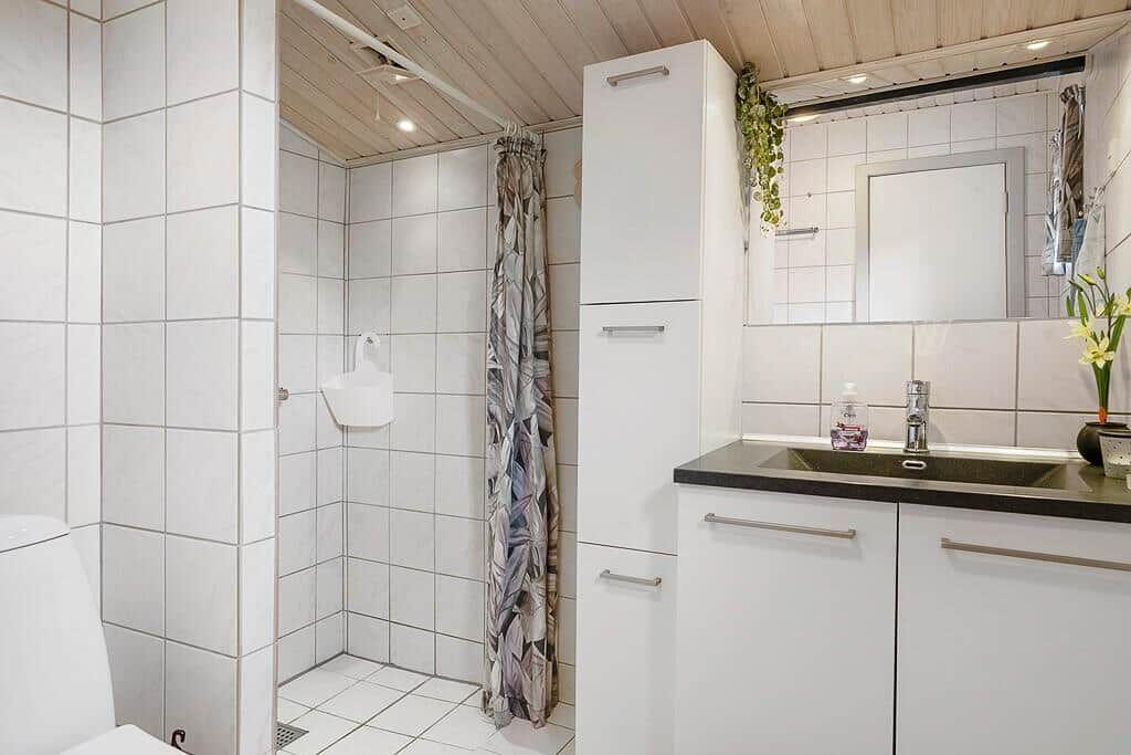 Badezimmer mit Dusche, Waschbecken und weißen Schränken.