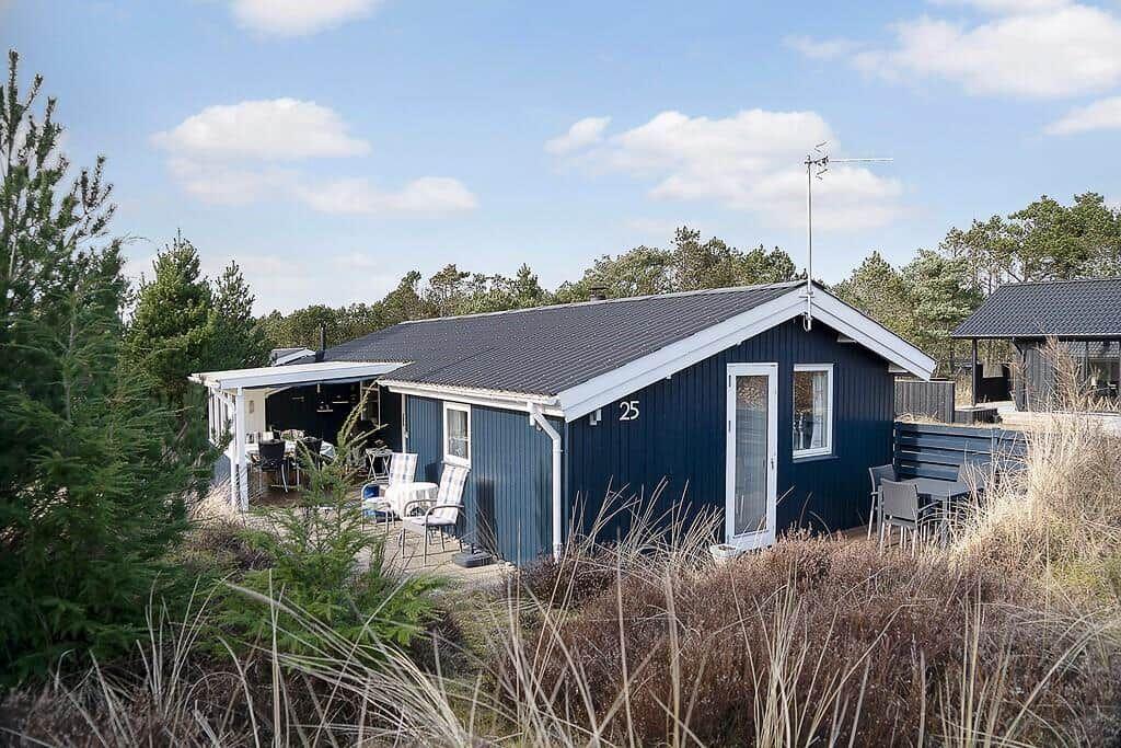 Blauer Holzblock mit Terrasse, Gartenmöbel und Antenne. Nummer 25. Umgeben von Bäumen und Gras.