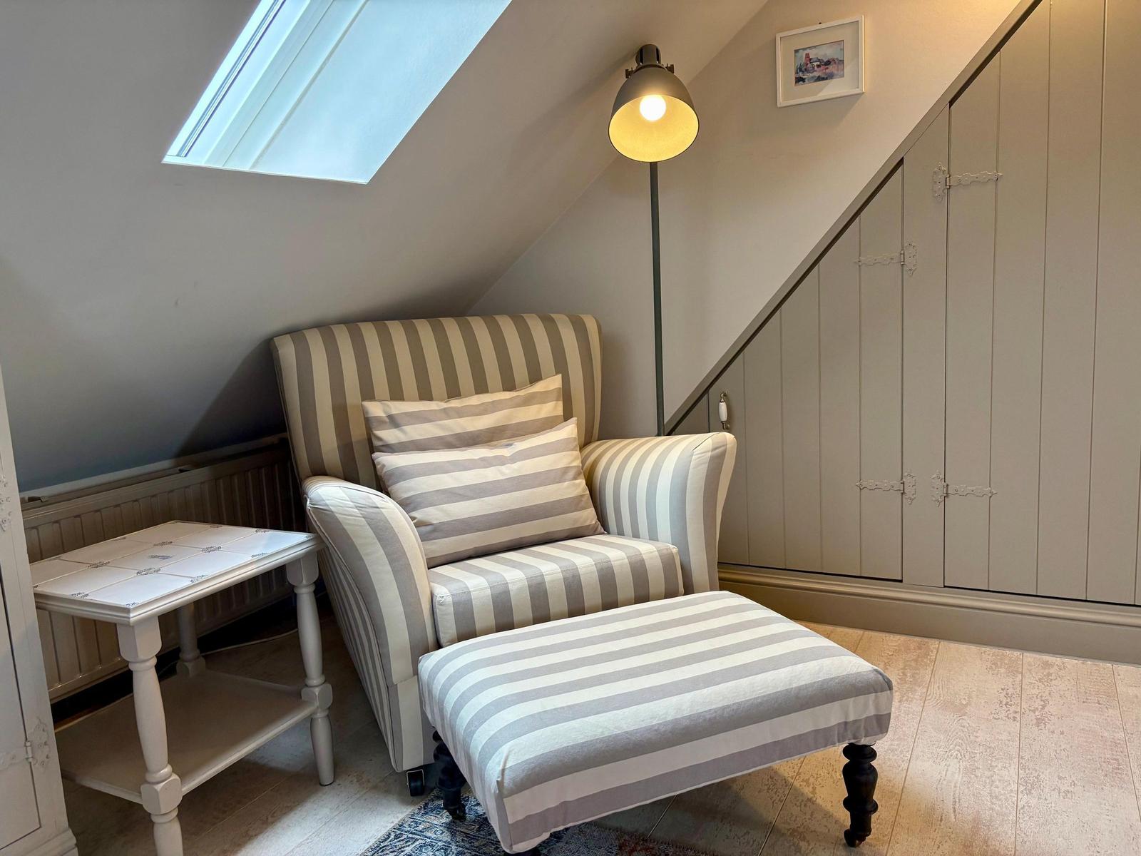 Seating area with striped armchair and footstool under sloped ceiling with skylight.