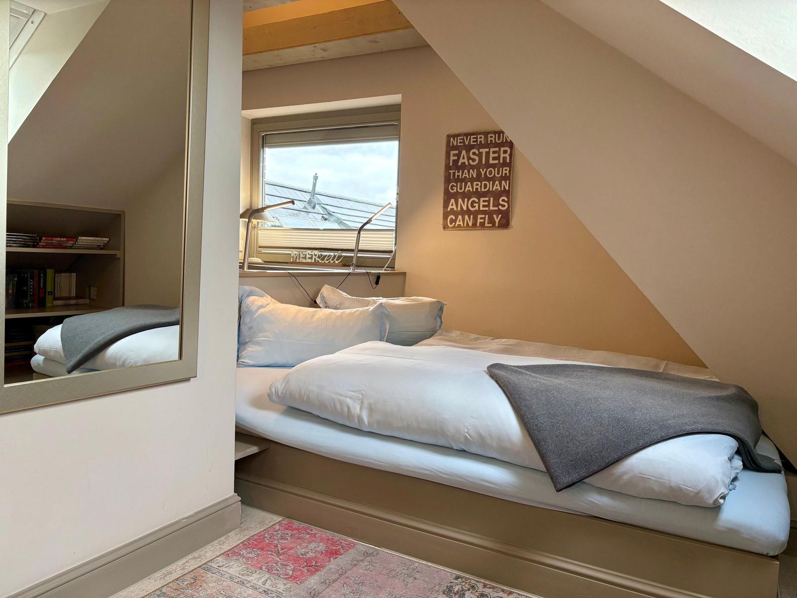 Bedroom with sloped ceiling, bed, window, and wall sign.