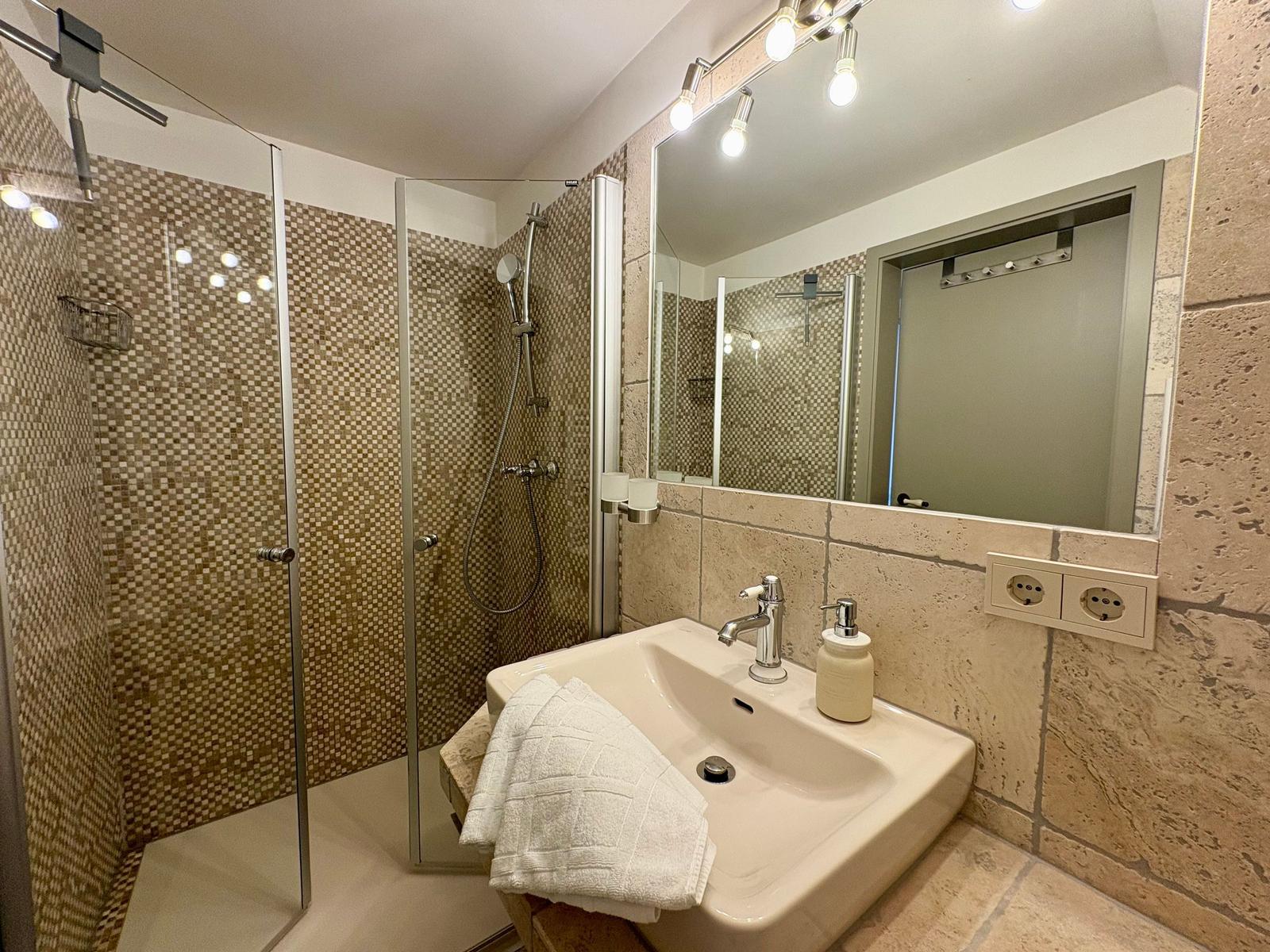 Bath with shower, sink, and mirror. Tile wall and wooden floor.