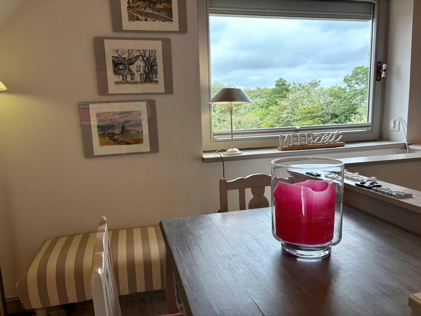 Table with candle, window view of forest, wall art, and lamp