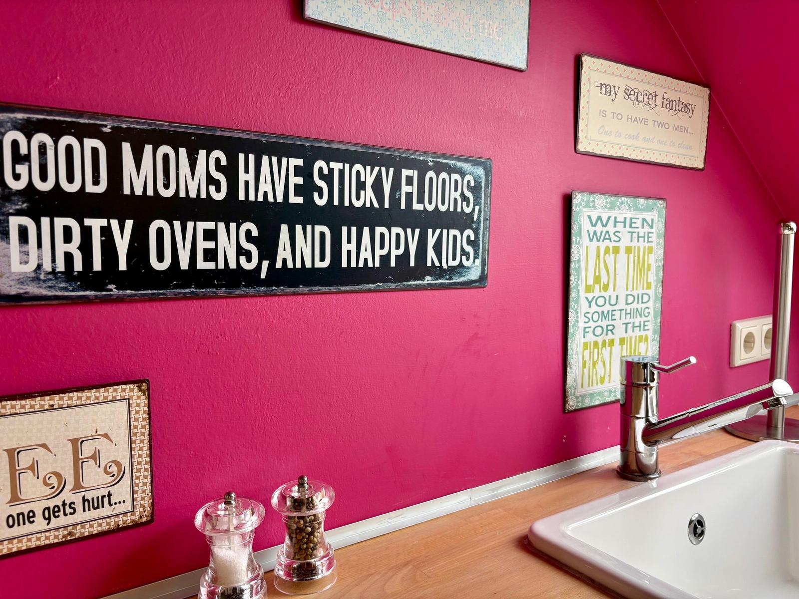 Pink kitchen wall with decorative signs above sink