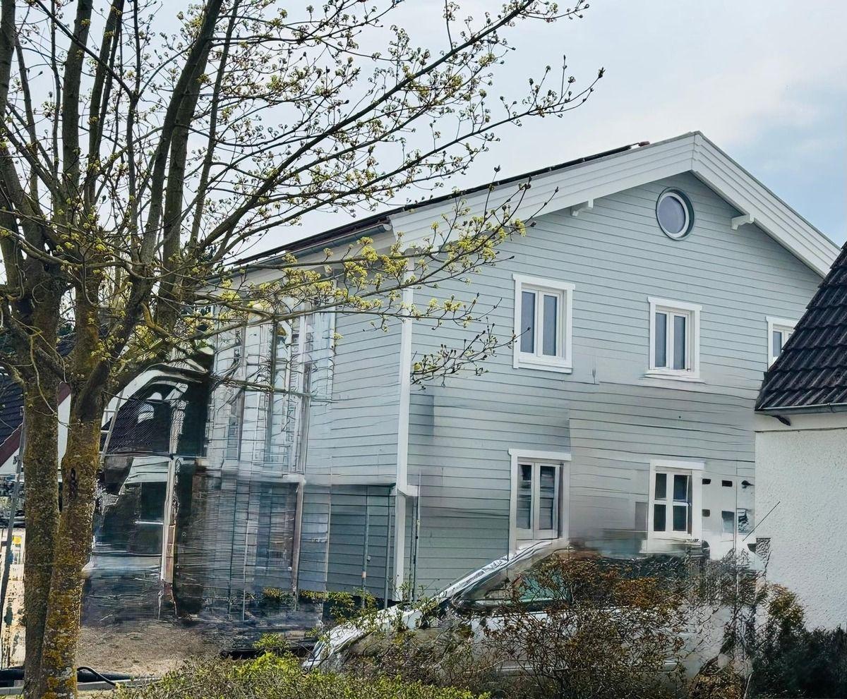 Ein zweistöckiges Haus mit hellblauen Wänden und weißen Fenstern. Ein Baum steht vor dem Haus.