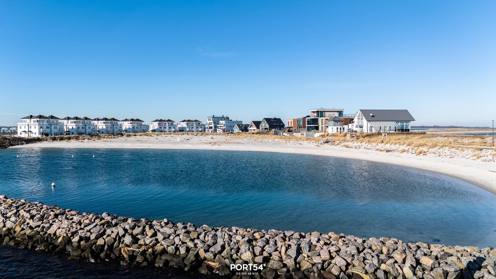 Strand mit Steinschutz und modernen Häusern im Hintergrund.