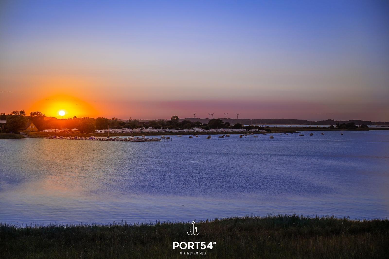 Sonnenuntergang über dem Wasser mit Booten und Windkraftanlagen im Hintergrund.