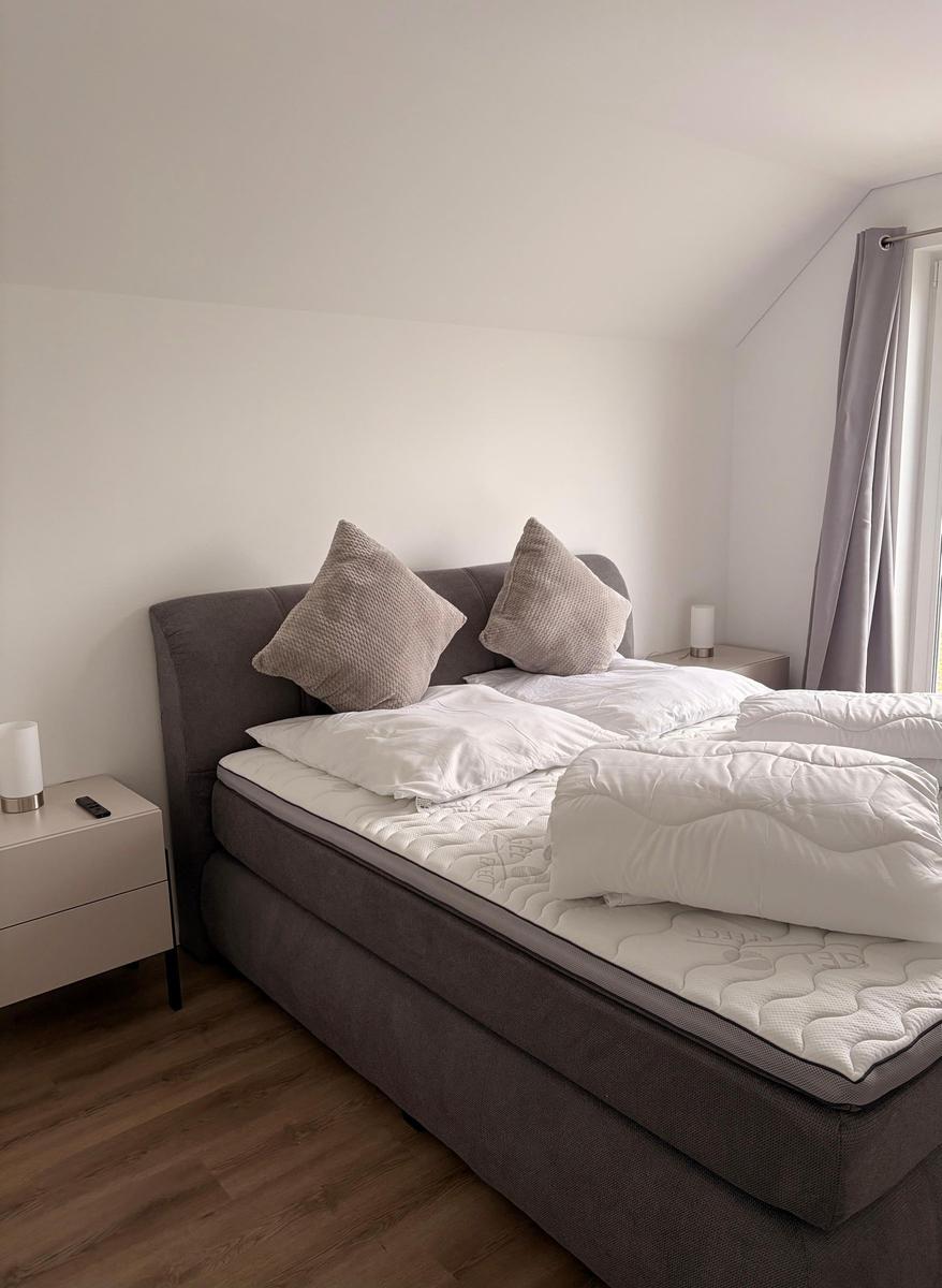 Schlafzimmer mit Doppelbett, Nachttischen und Fenster mit Vorhängen.