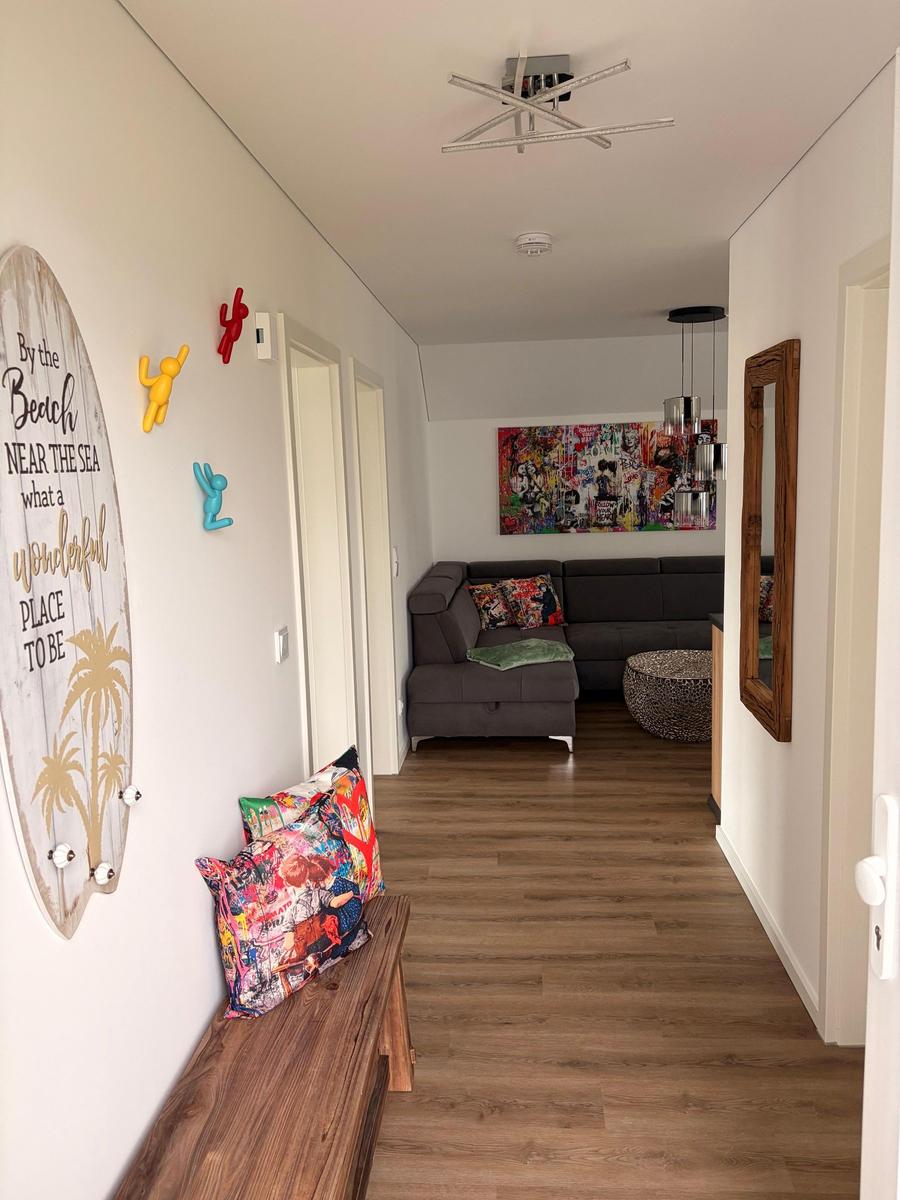 Flur mit Holzboden, Wanddekoration und Blick in Wohnzimmer mit Sofa und Wandbild.