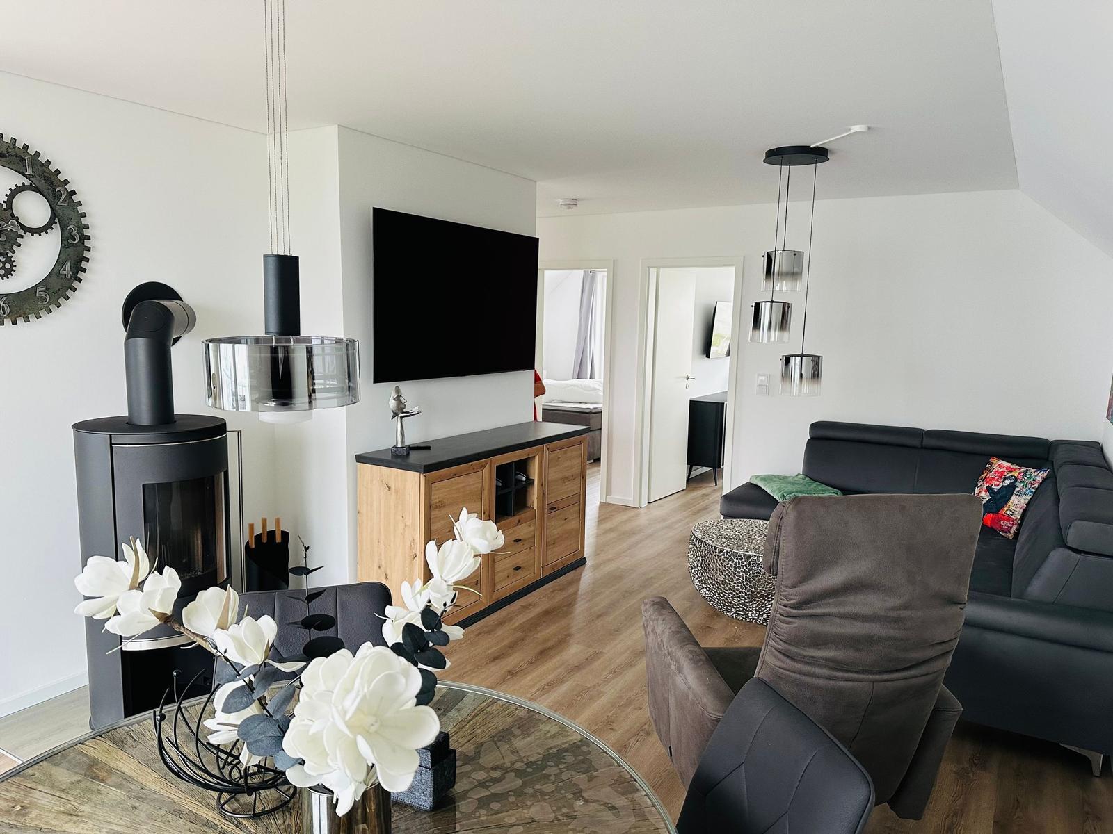Wohnzimmer mit Sofa, Kamin und Fernseher. Holzboden und moderne Beleuchtung.