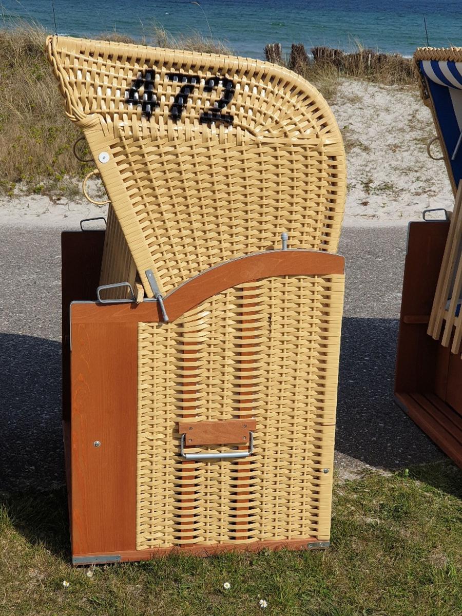 Strandkorb mit Nummer 472 auf Gras vor Strand