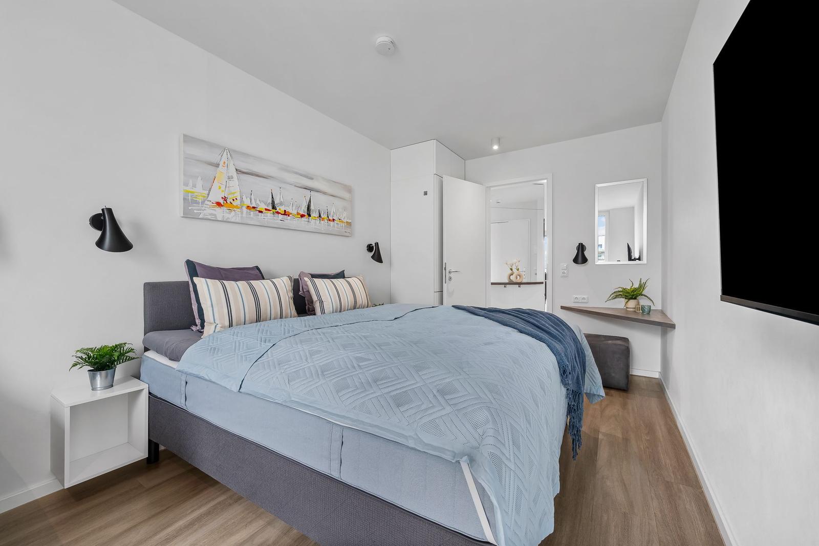 Schlafzimmer mit Bett, Wandbild, Schreibtisch und Fernseher.