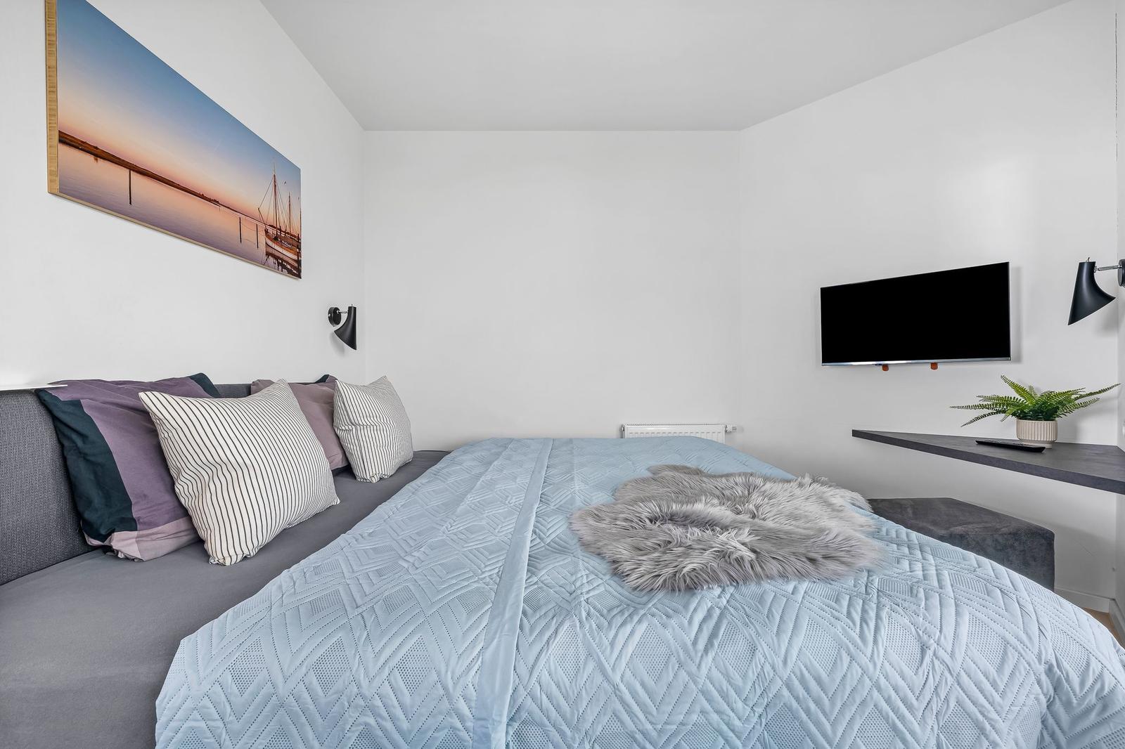 Schlafzimmer mit Bett, Wandbild, Fernseher und Pflanze.