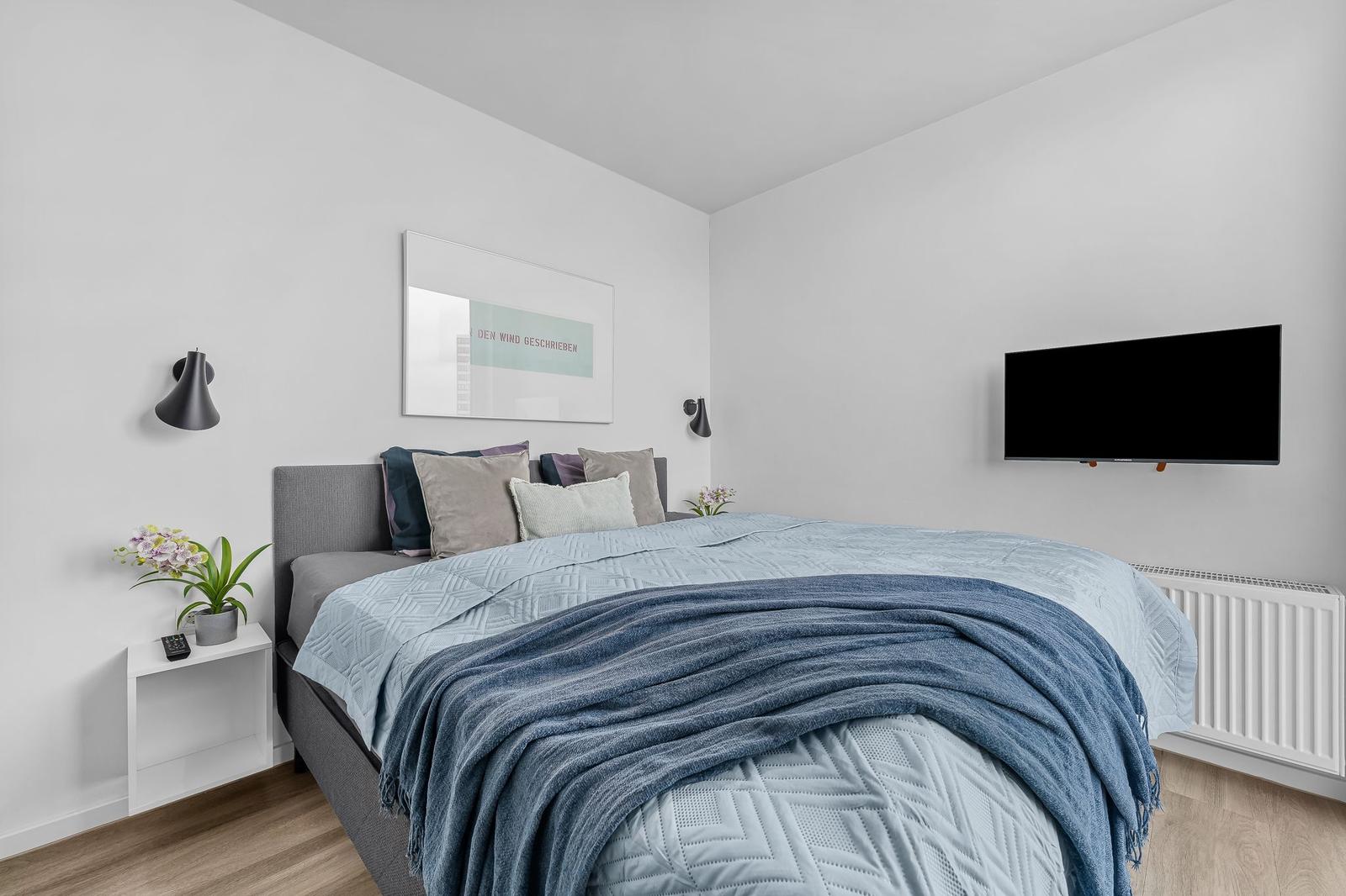 Schlafzimmer mit Bett, Wandbild und Fernseher.