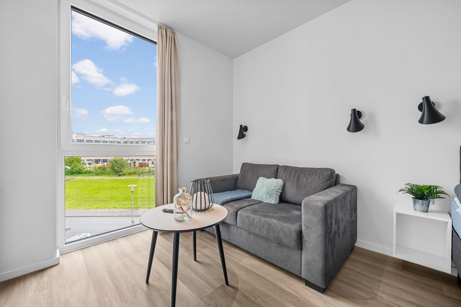 Wohnzimmer mit Sofa, Tisch und Blick auf Grünfläche.