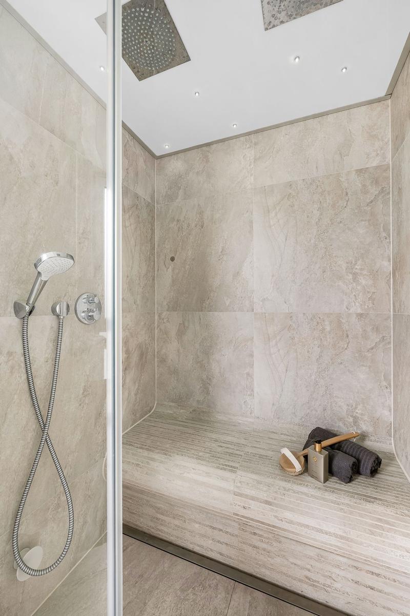 Duschkabine mit Dachdusche, Handbrause und Sitzbank aus Steinfliesen.