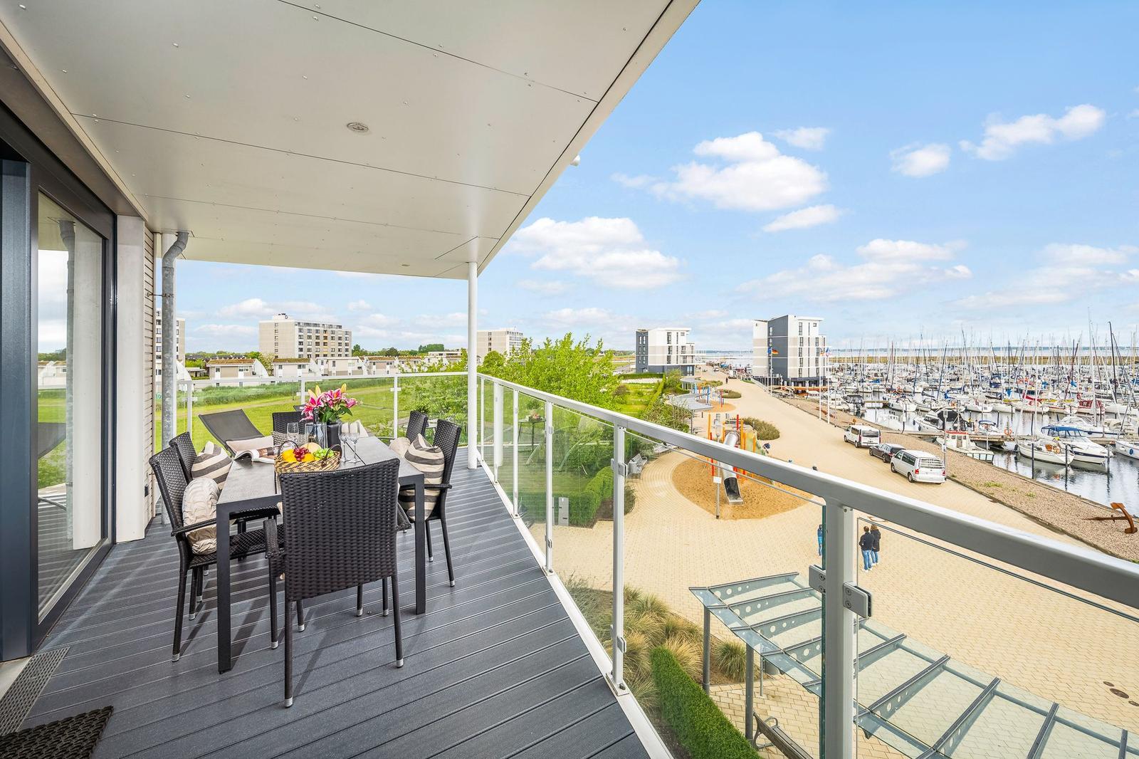 Terrasse mit Tisch, Stühlen und Blick auf Hafen und Strand.