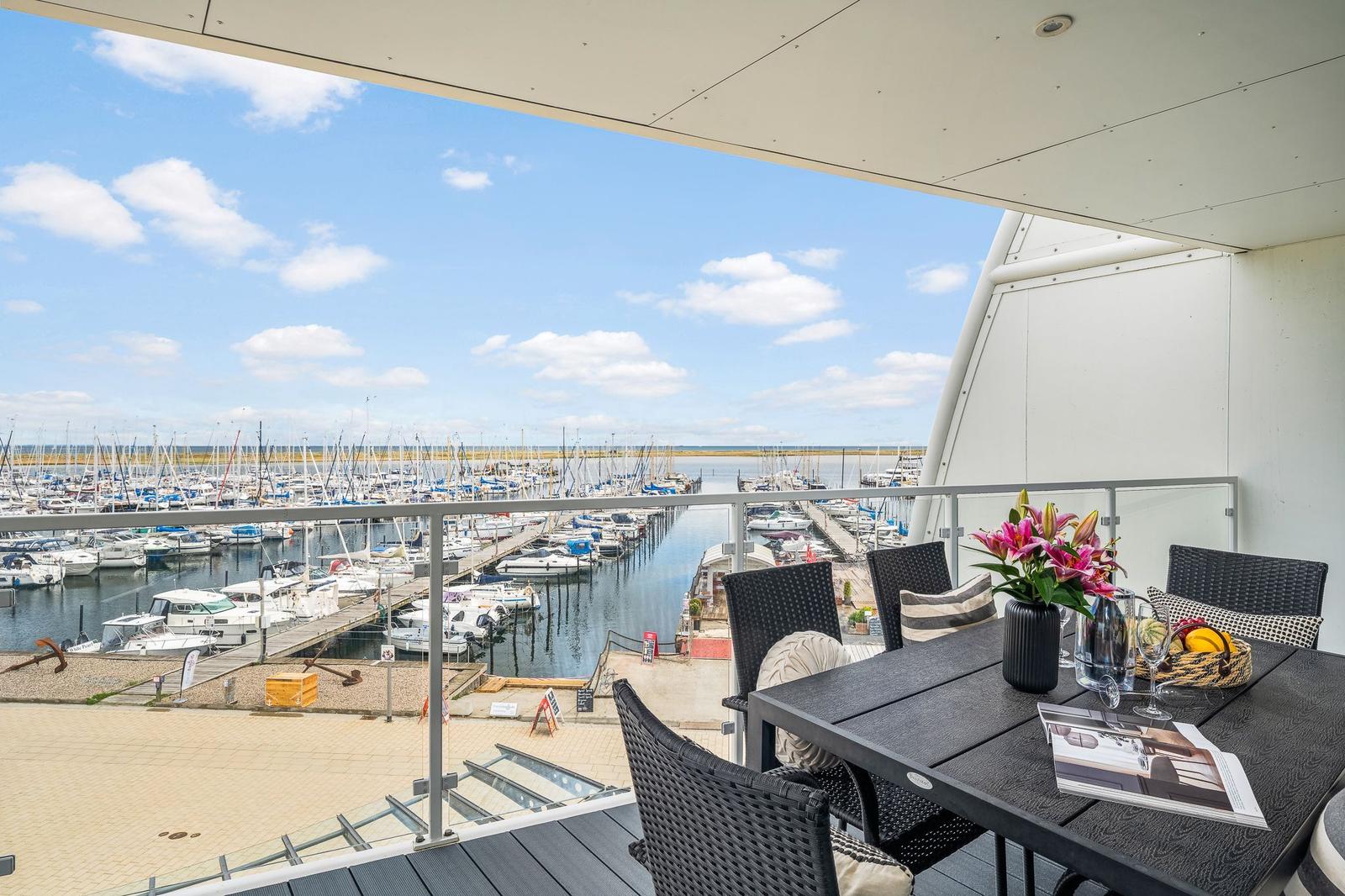Terrasse mit Tisch und Stühlen bietet Blick auf Hafen mit Booten.