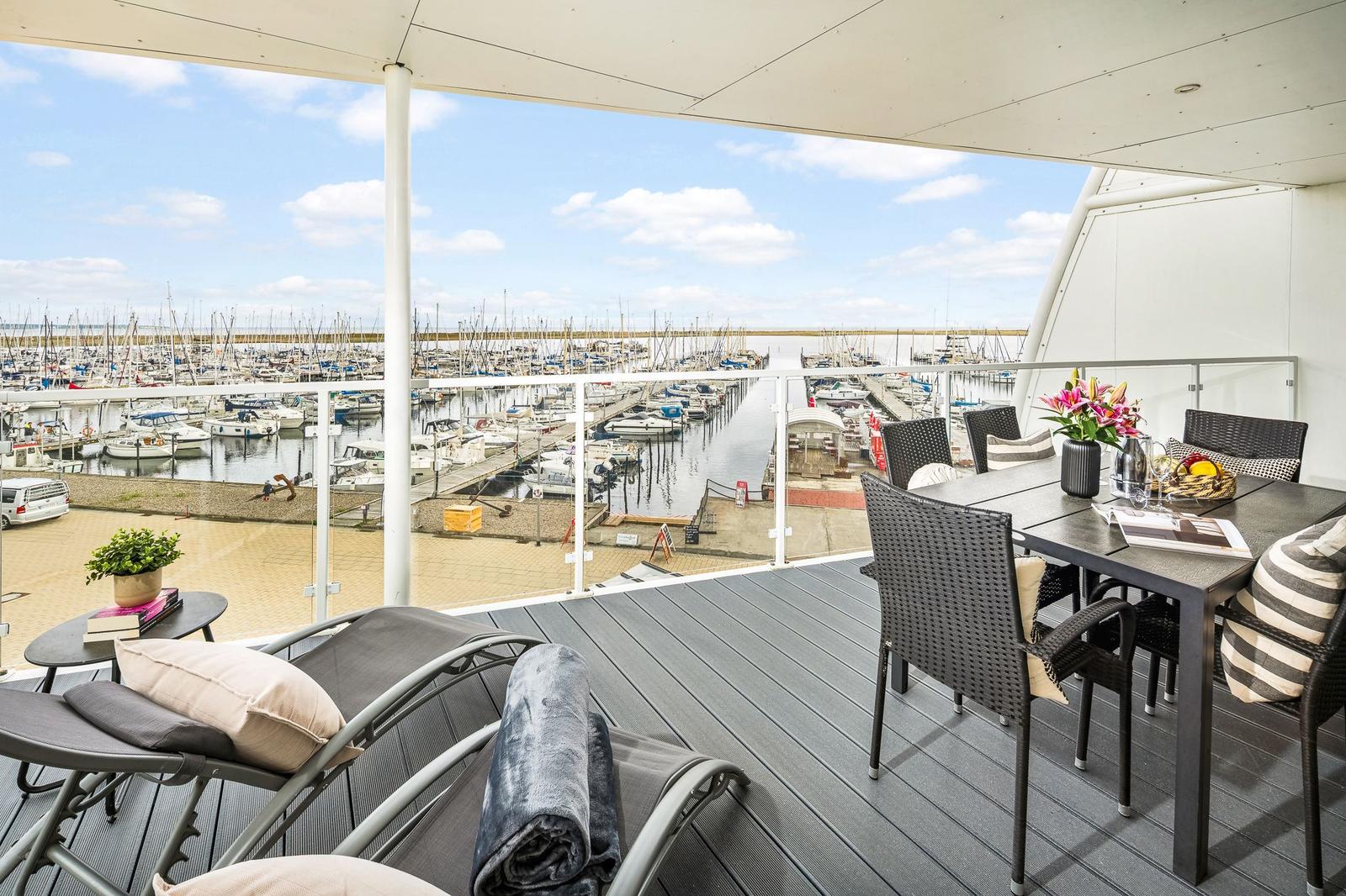 Terrasse mit Tisch, Stühlen und Blick auf Hafen mit Booten.