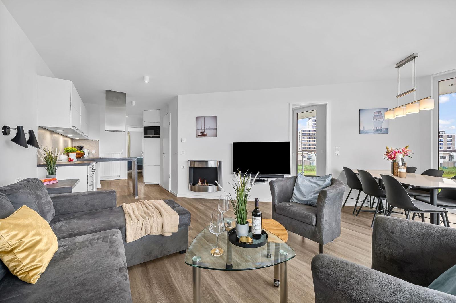 Wohnbereich mit Sofa, Sessel, Esstisch und Küche. Kamin und Fernseher im Zentrum.