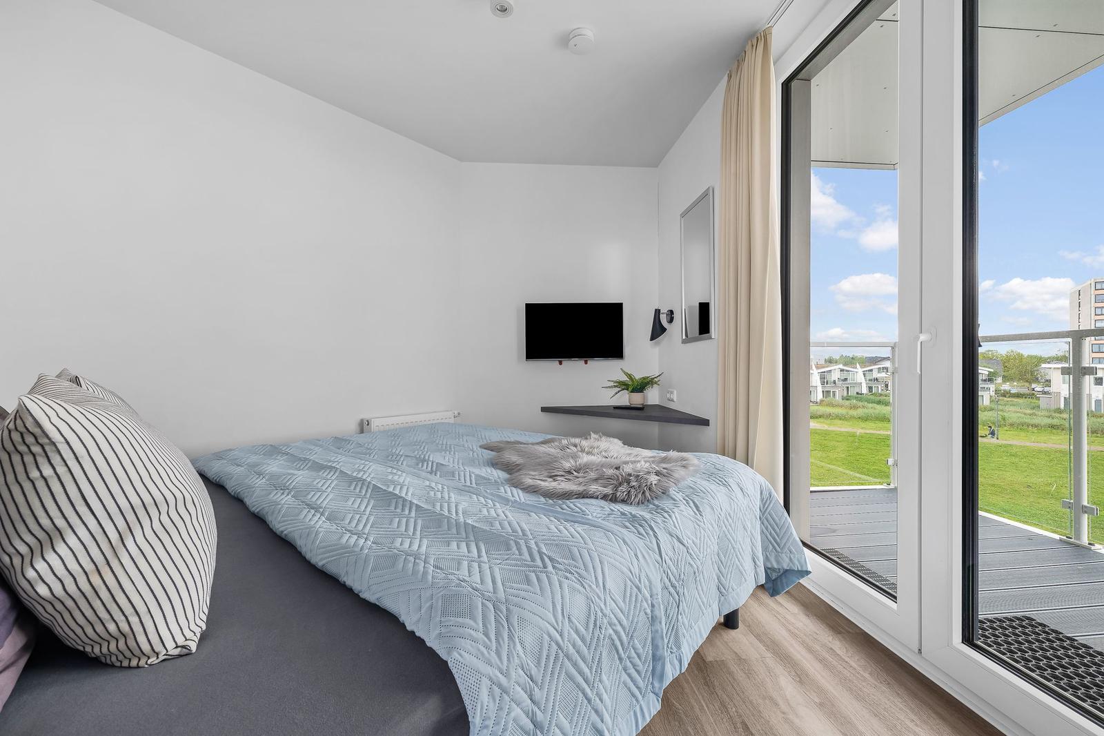 Schlafzimmer mit Bett, TV und Balkonansicht