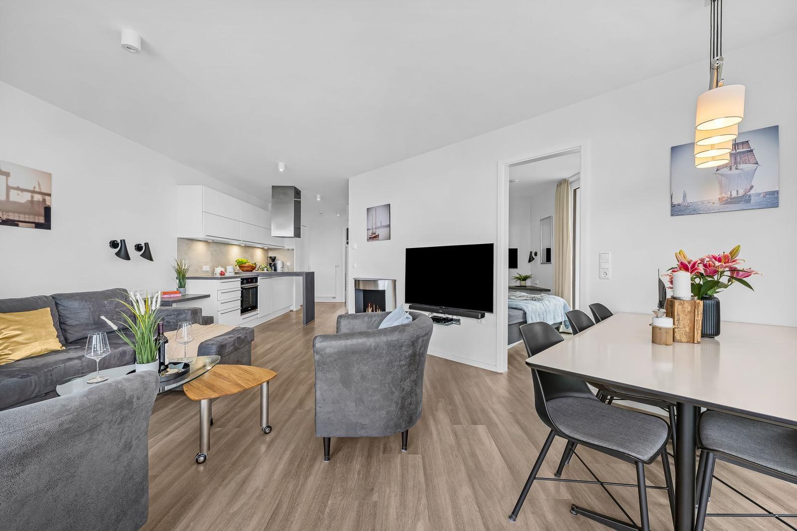 Wohnbereich mit Küche, Esstisch und Fernseher. Schlafzimmer im Hintergrund.