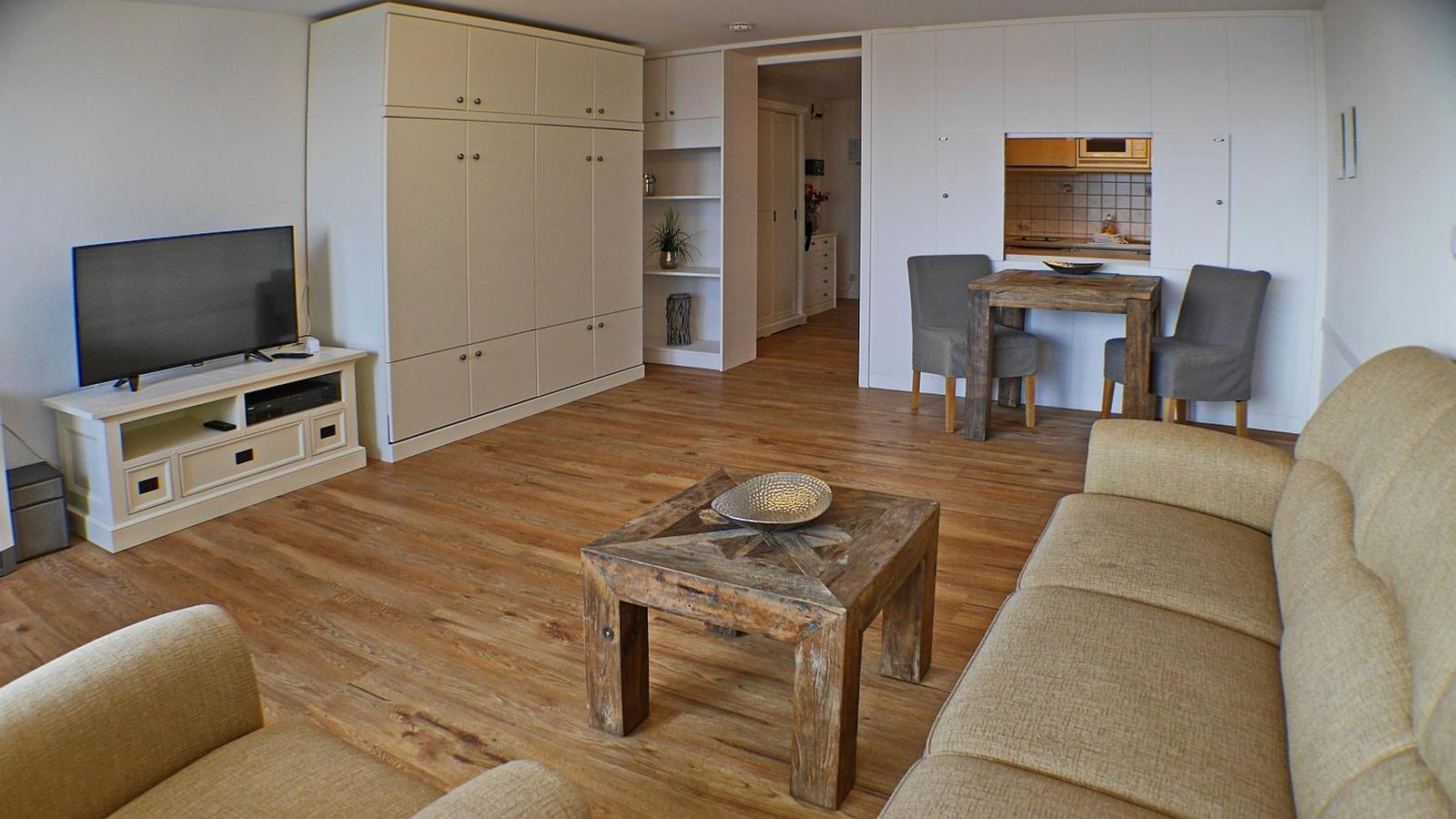 Wohnzimmer mit Sofa, Couchtisch, TV und Küchenbereich im Hintergrund.