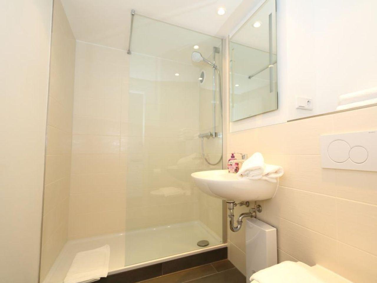 Dusche mit Glaswand, Waschbecken und Toilette in einem hellen Badezimmer.