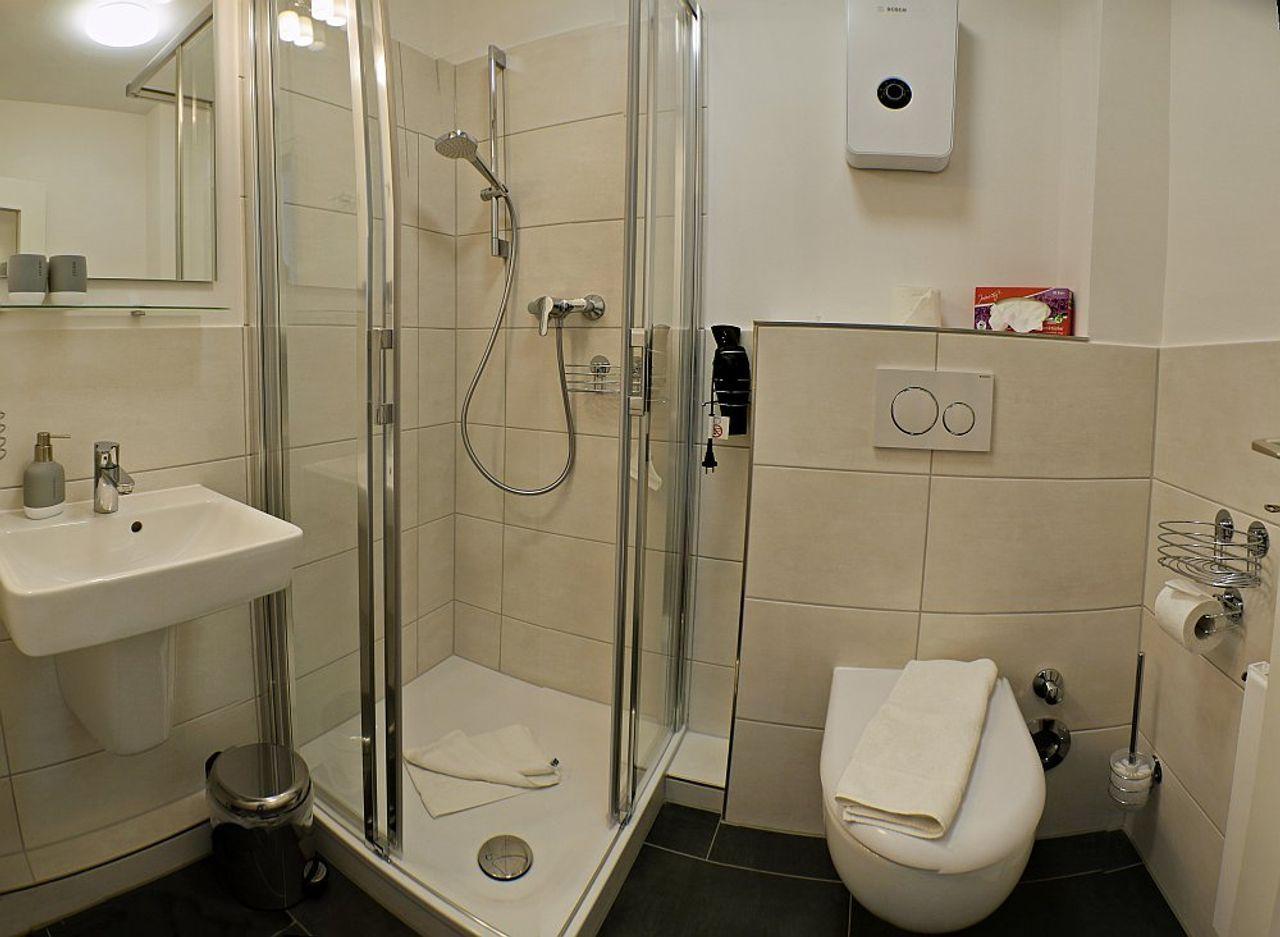 Badezimmer mit Dusche, Waschbecken und WC. Fliesen und weiße sanitäre Einrichtung.